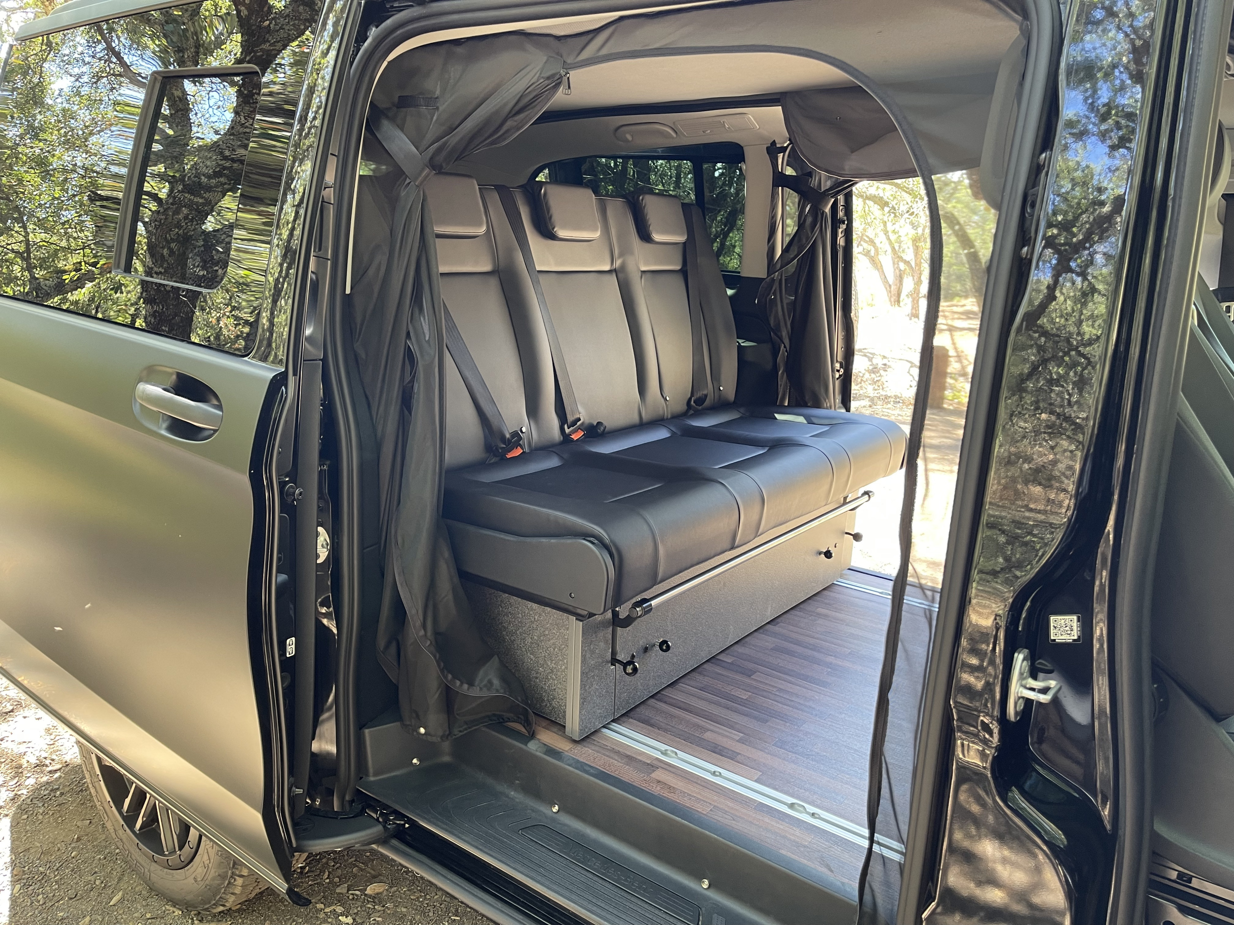Black leather three-seat bench in an RV rental van, converting to a bed with storage below and wood-look floor.. Mercedes-Benz Metris 2020