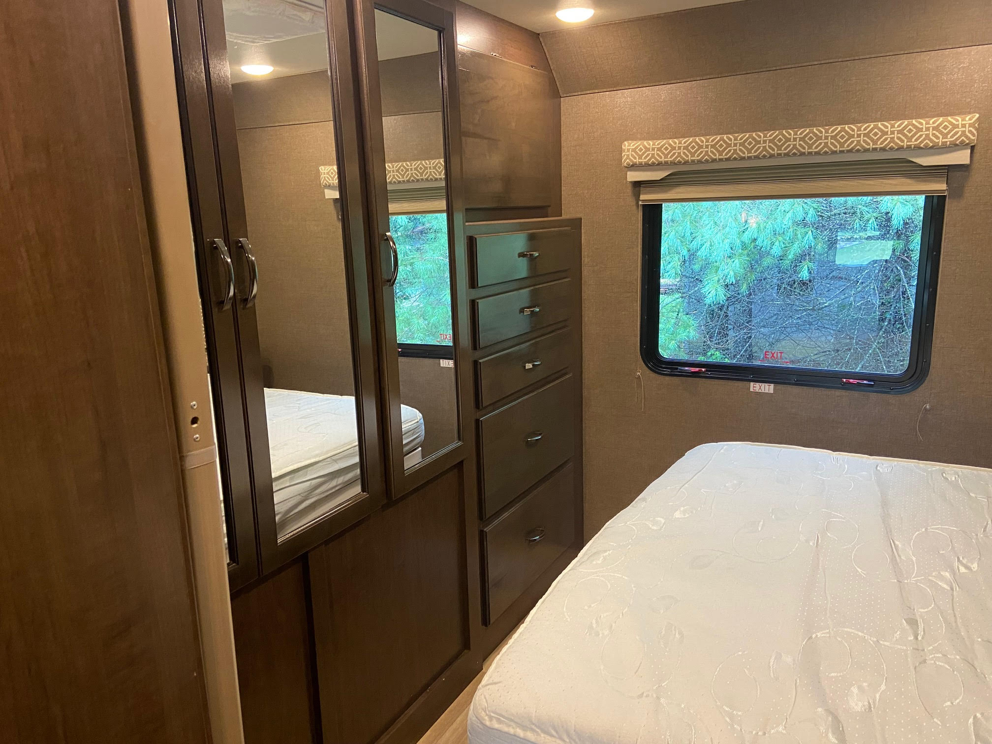 RV rental bedroom interior: a mirrored wardrobe, built-in dresser, bed, and window with an outdoor view.. Thor Motor Coach Freedom Elite 2017