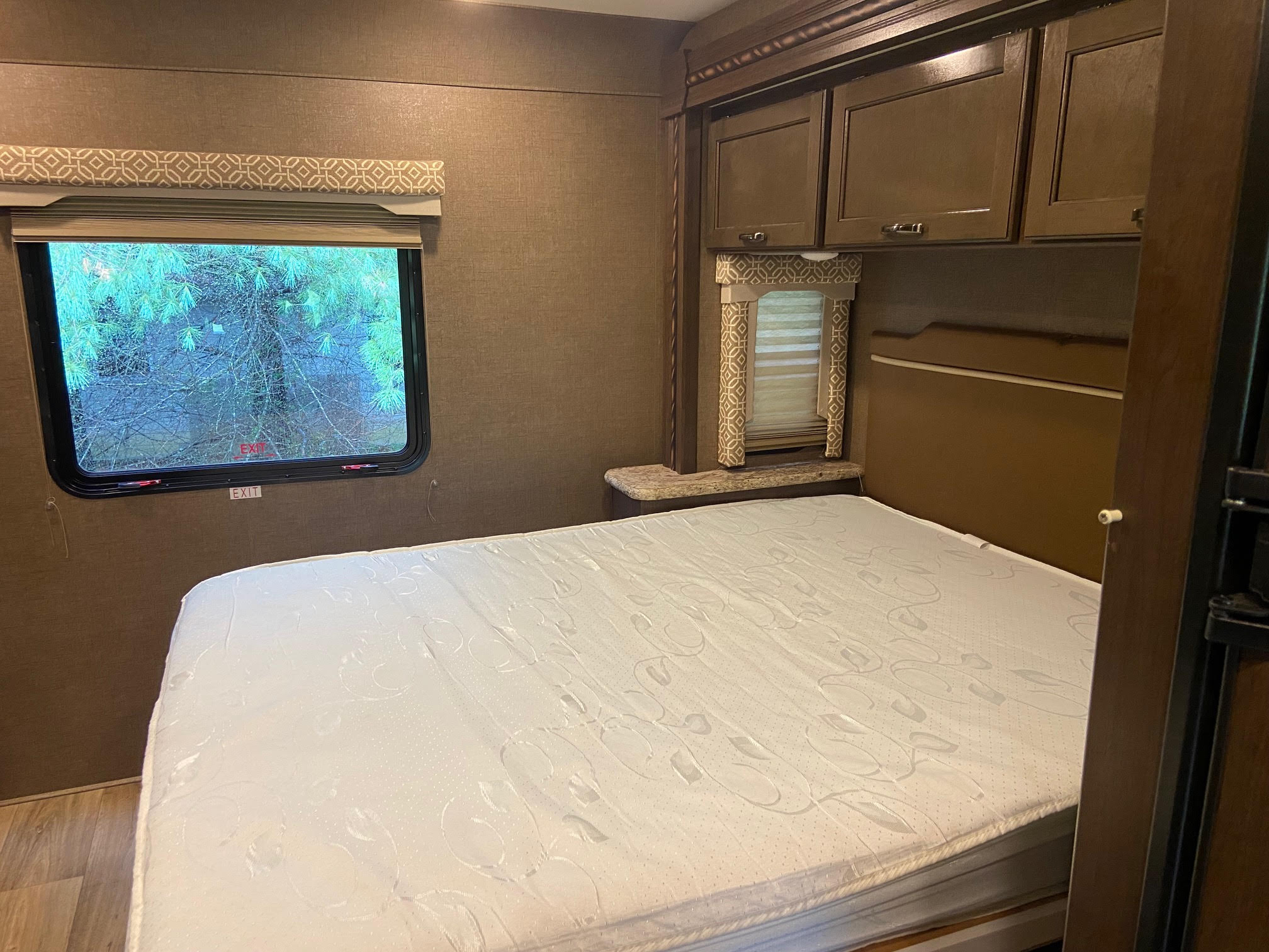 Spacious RV rental bedroom featuring a clean white mattress, large window, and overhead storage cabinets.. Thor Motor Coach Freedom Elite 2017