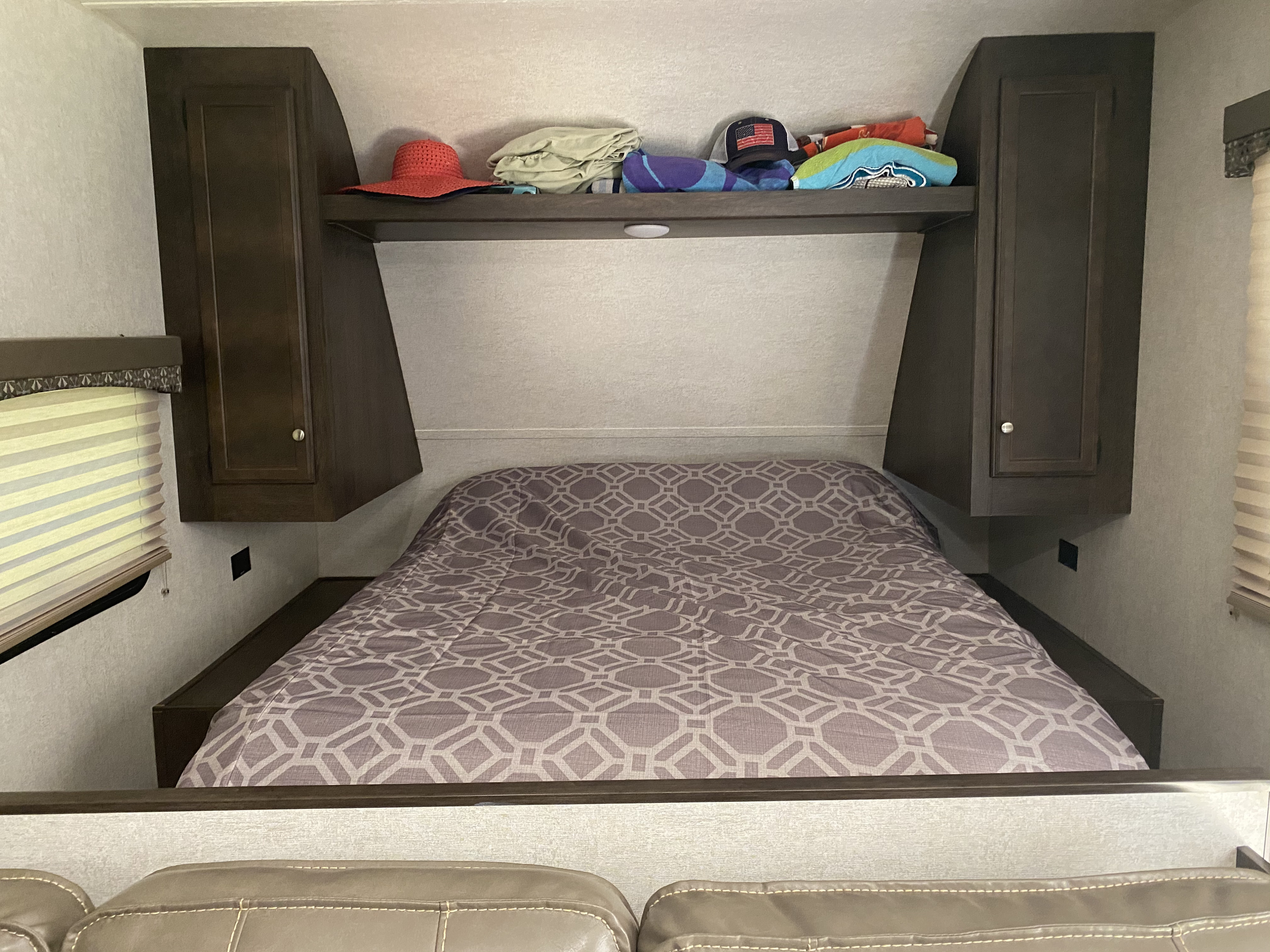 RV rental bedroom with a comfy, patterned bed, dark wood overhead cabinets, and shelf storage. Ideal for a cozy camper stay.. Starcraft Autumn Ridge 2018