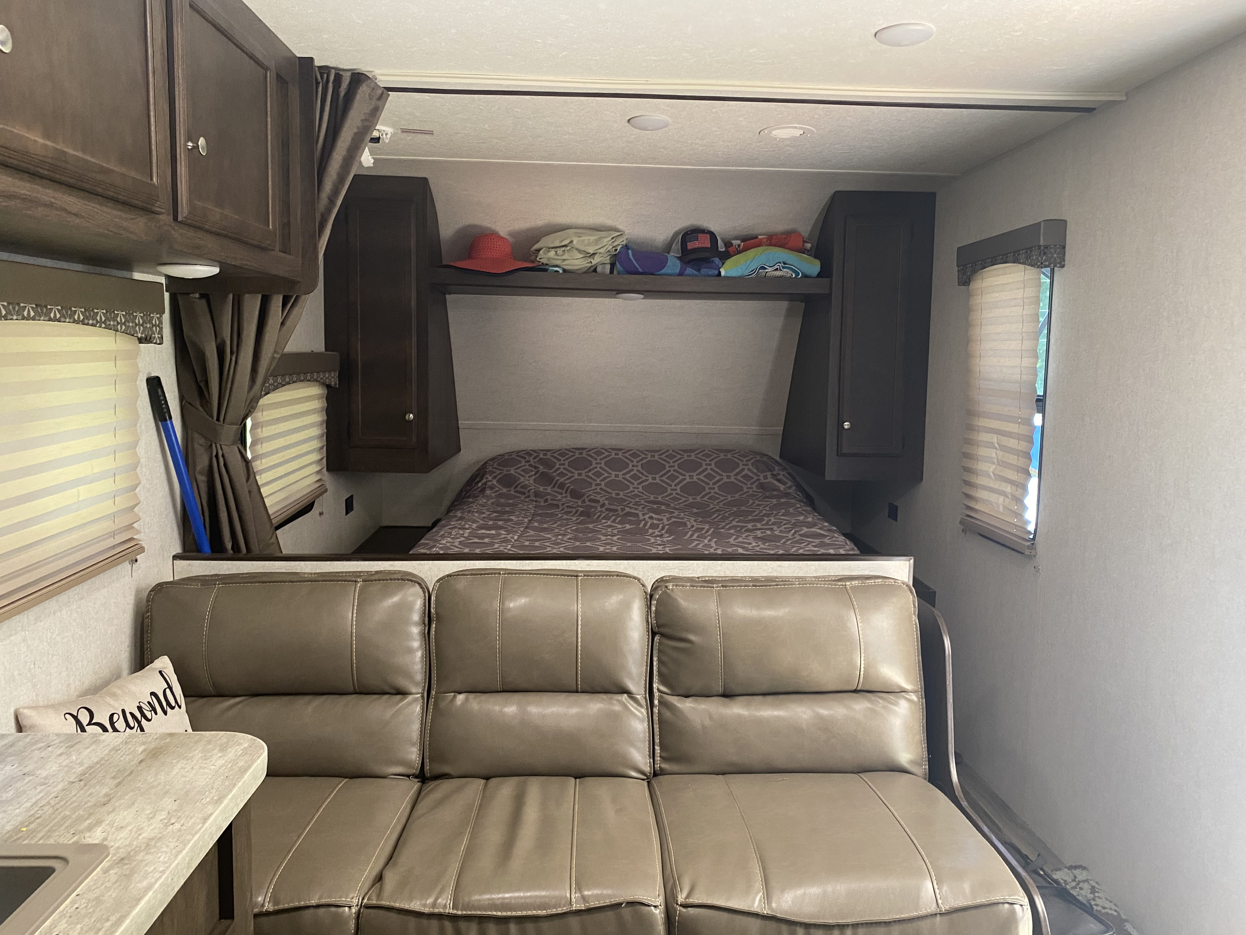 Cozy interior of an RV rental, featuring a tan sofa, a bed with patterned cover, and overhead storage cabinets.. Starcraft Autumn Ridge 2018