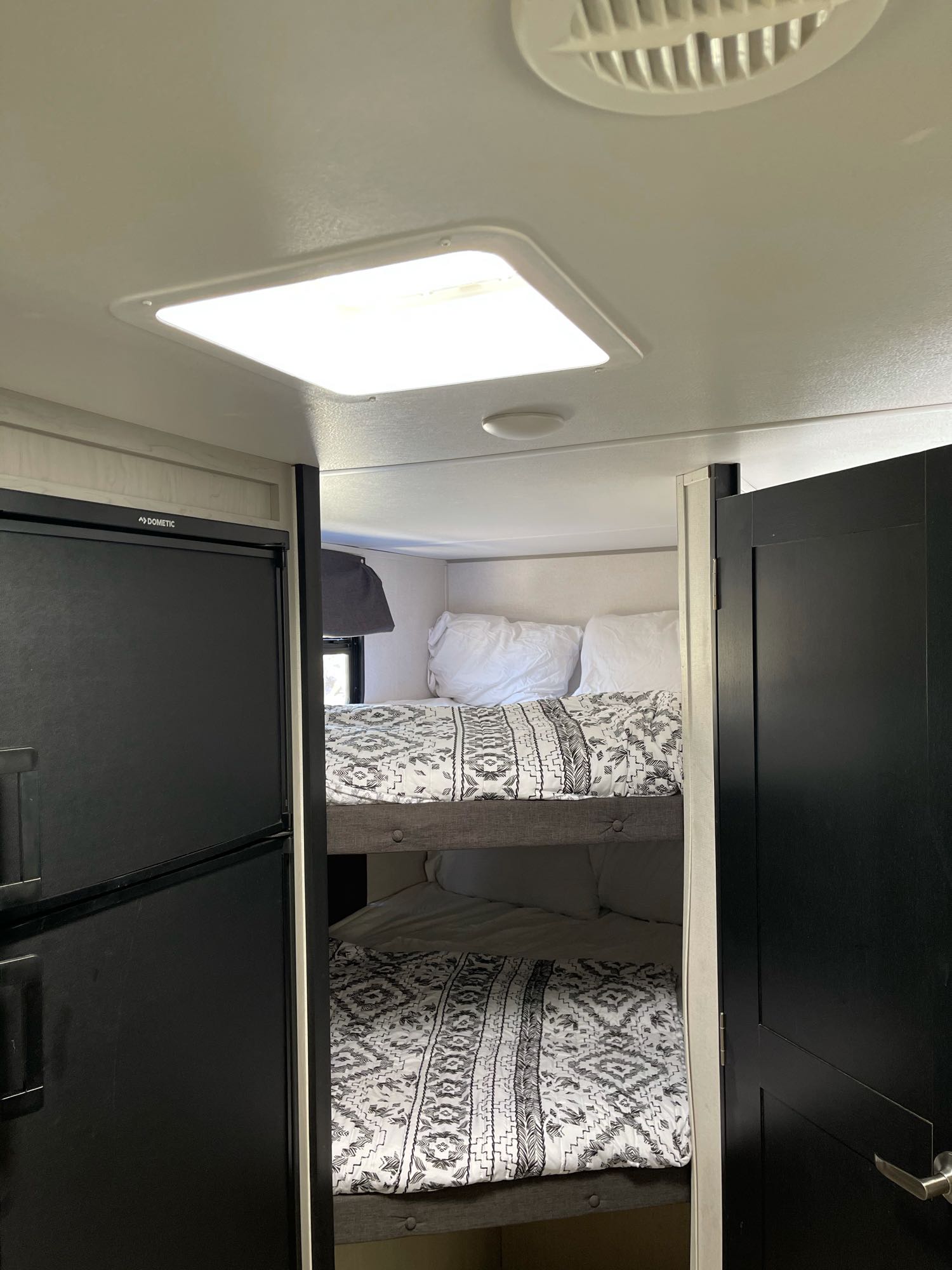 Interior of an rv rental featuring two bunk beds with patterned bedding, a Dometic refrigerator, and a dark bedroom door.. Prime Time Tracer 2021