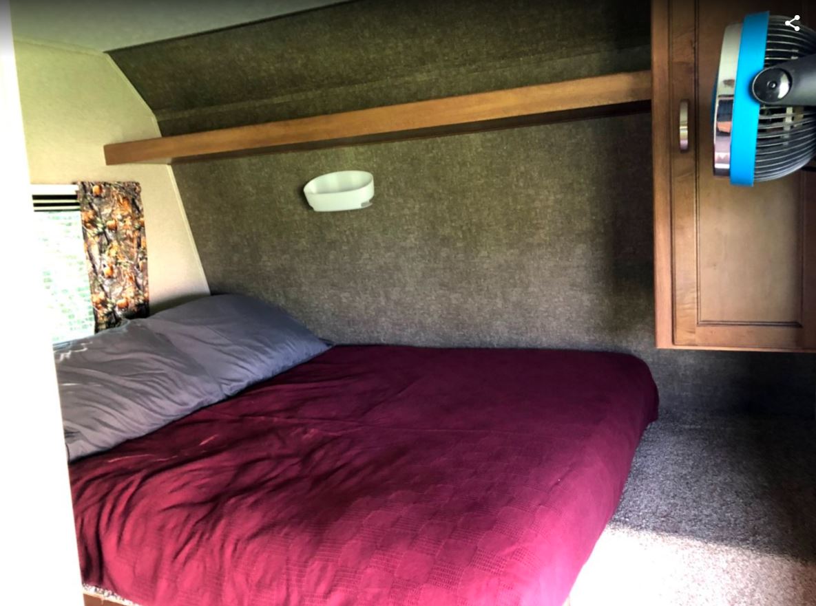 Inside this RV rental, a compact bedroom offers a bed, camo curtains, storage, and a fan for comfort.. Other Other 2018