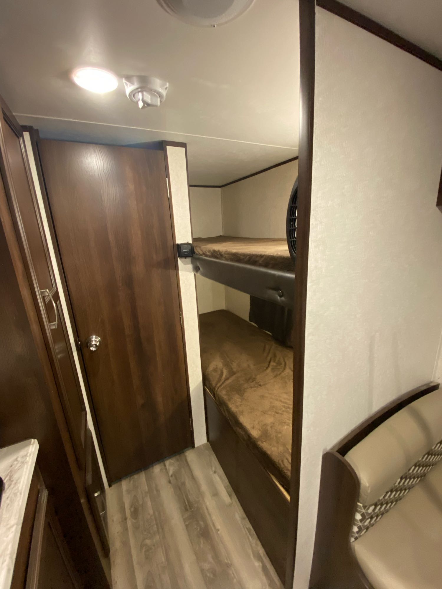 Inside an **rv rental**, showing cozy bunk beds, a wooden door, and part of a cream-colored bench seating area.. Jayco Baja 2020