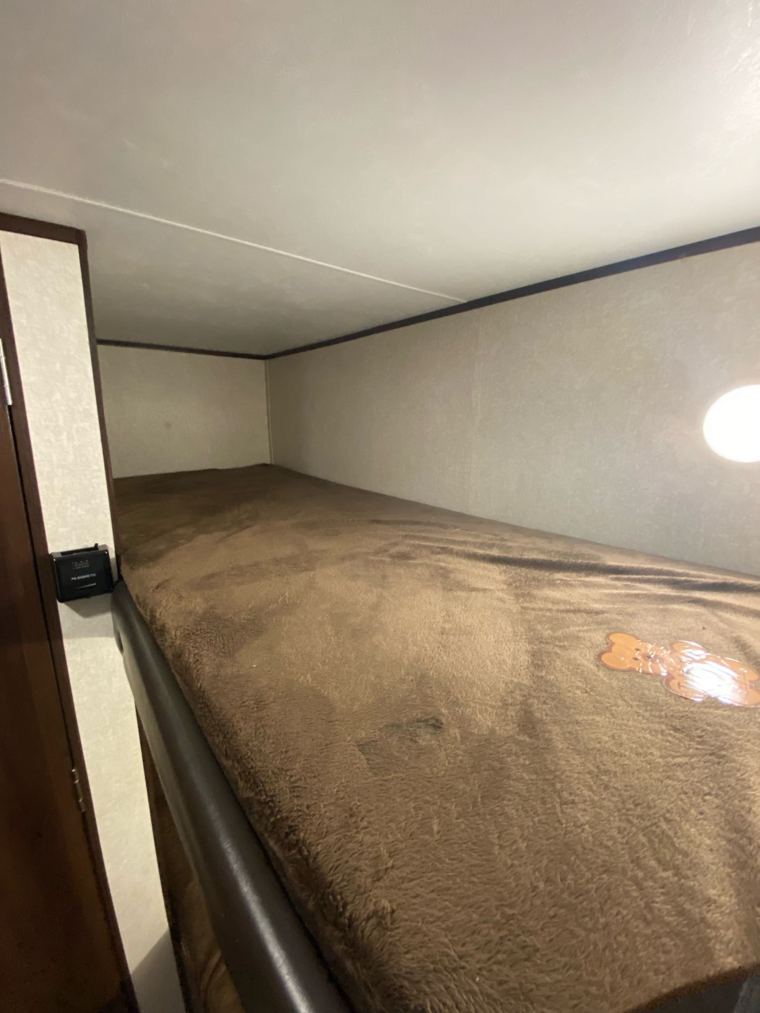 View inside an RV rental showing a lower bunk bed with a brown fleece blanket & wall-mounted light.. Jayco Baja 2020