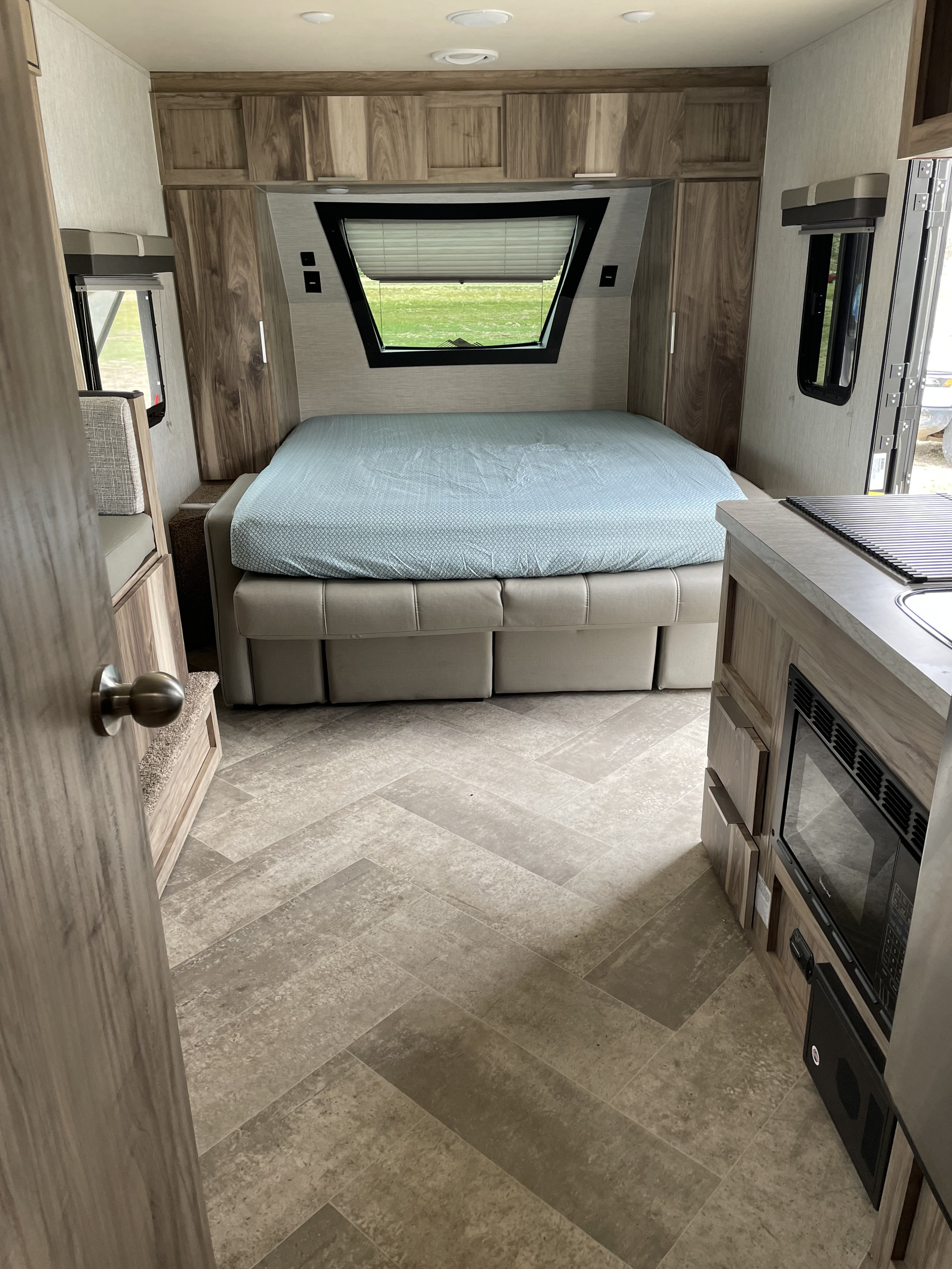 RV rental interior featuring a neat bedroom with a bed & cabinets, alongside a compact kitchen area and modern flooring.. Other Other 2021
