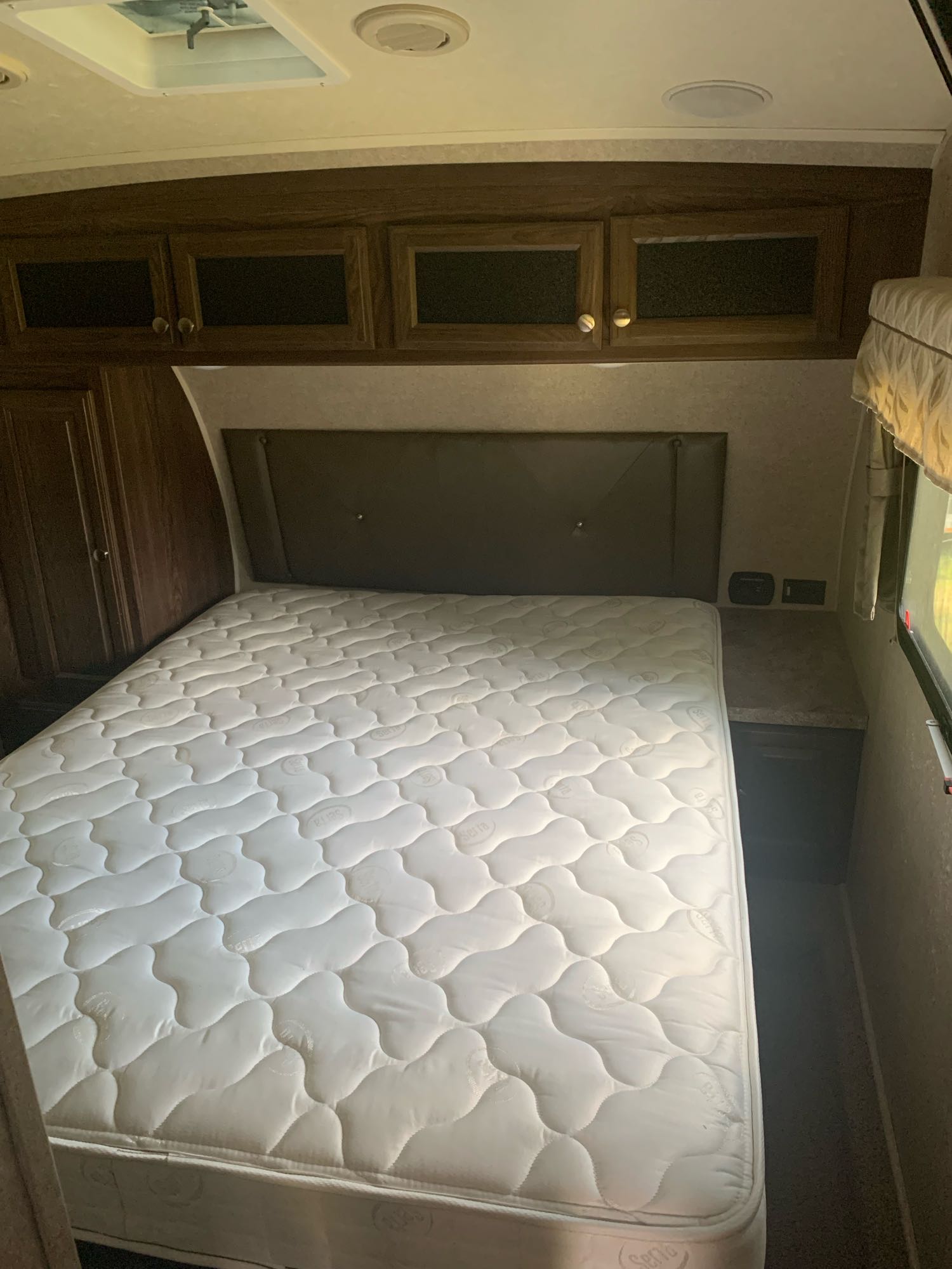 Cozy RV rental bedroom featuring a white mattress, padded headboard, wood cabinets, and bedside storage.. Flagstaff Classic Super Lite 2017