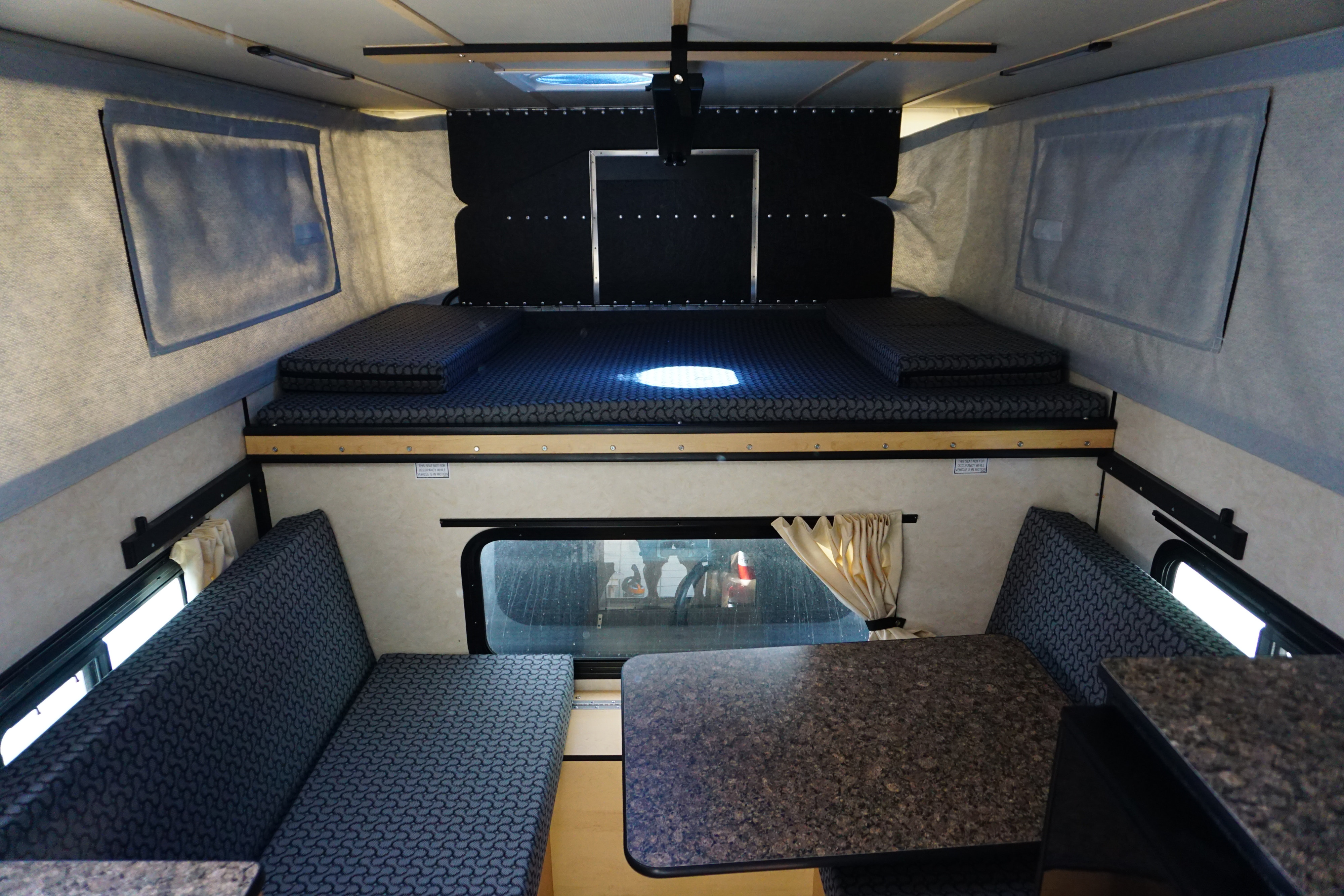 Inside a clean RV rental, featuring an upper bed and lower dinette with seating and a table.. Chevrolet silverado 2018