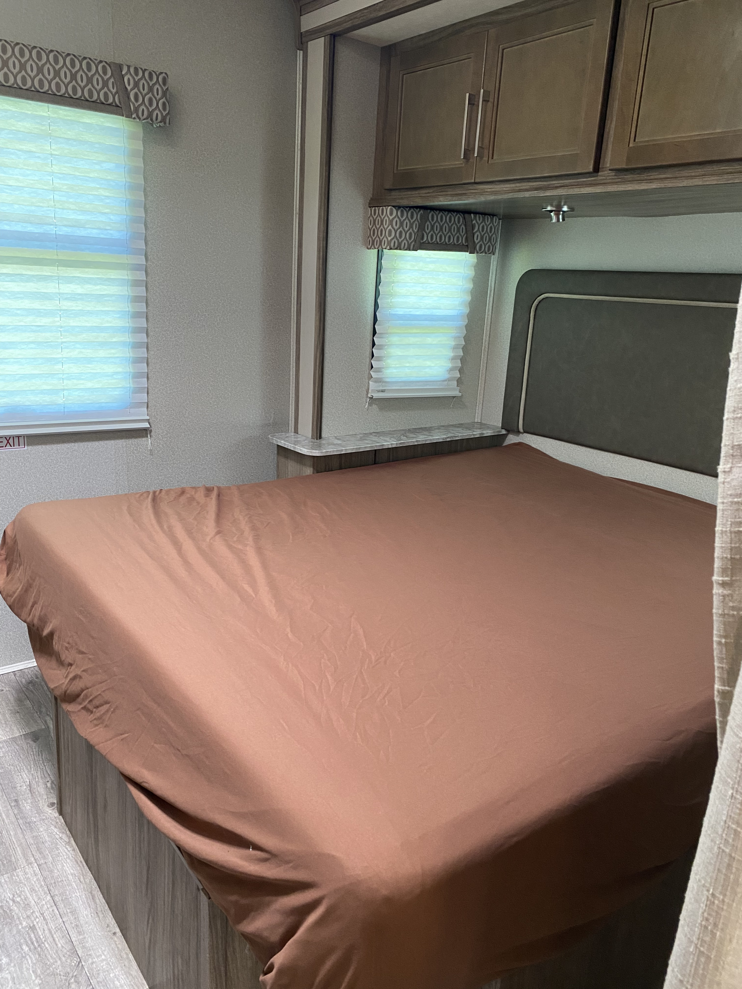 Comfortable RV rental bedroom with a cozy bed, windows, overhead cabinets, and built-in shelving. Ideal for travel comfort.. Entegra Coach Other 2018
