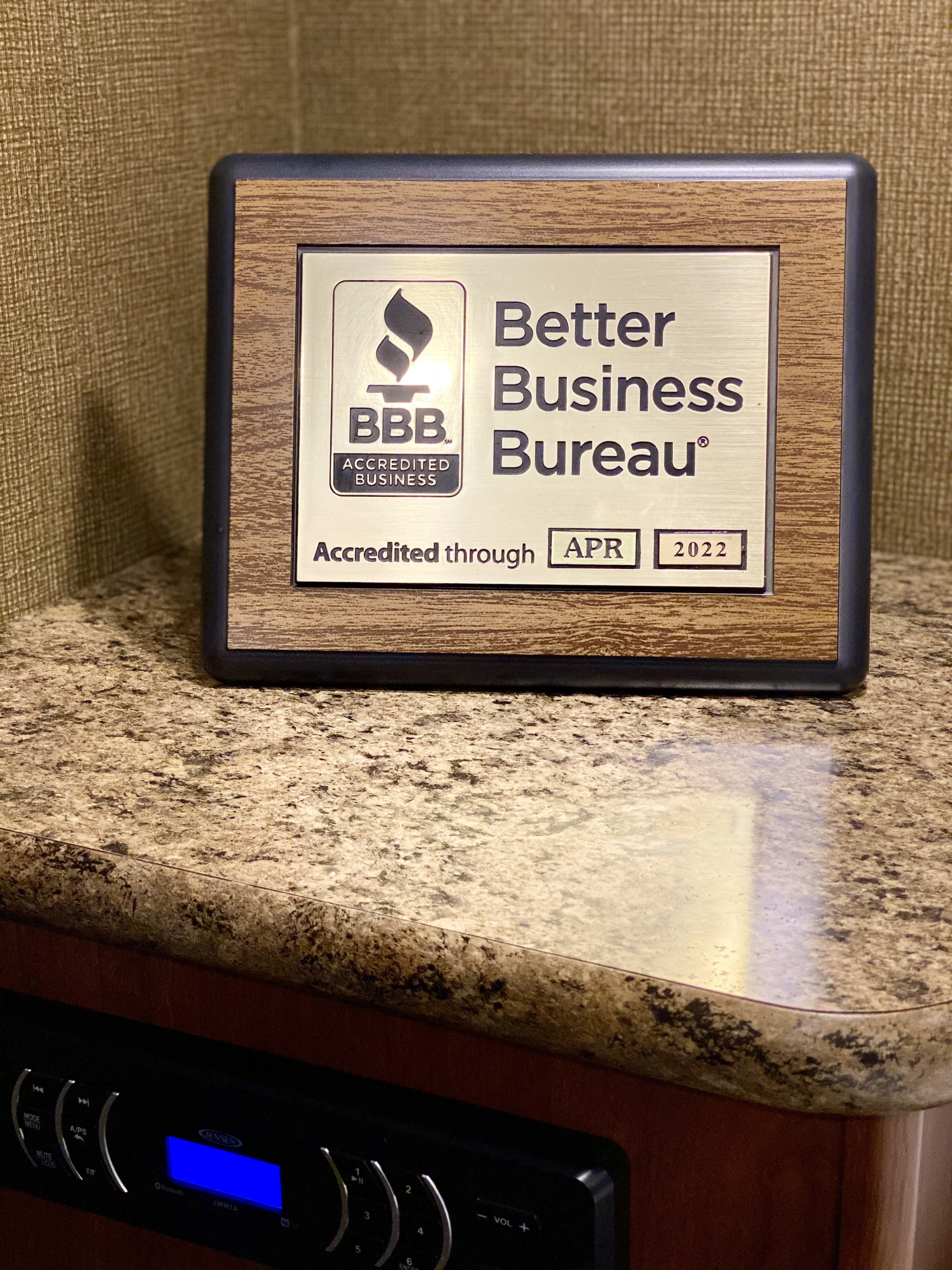 An RV rental's BBB plaque, accredited through APR 2022, rests on a counter above a Jensen stereo system.. Forest River Cherokee Grey Wolf 2019