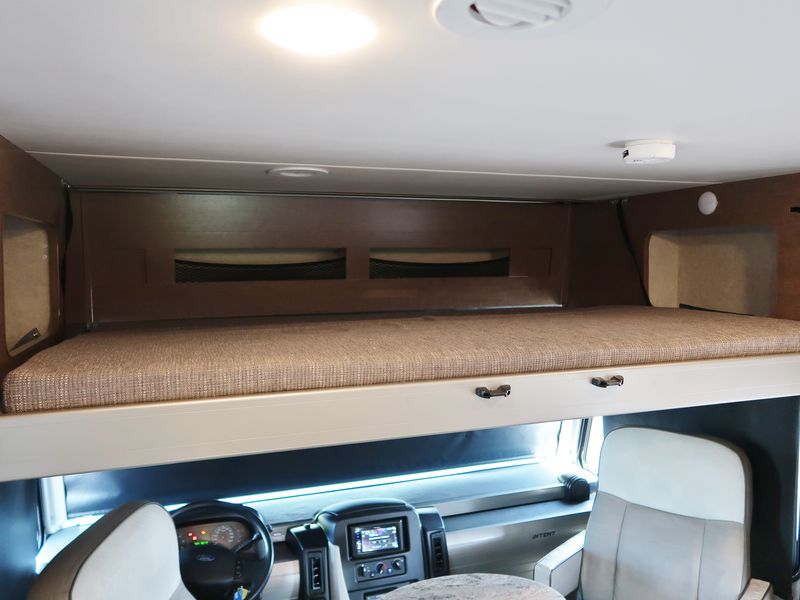 RV rental interior with a spacious cabover bed above the driving area, showing the steering wheel and passenger seat.. Winnebago Winnebago 2020