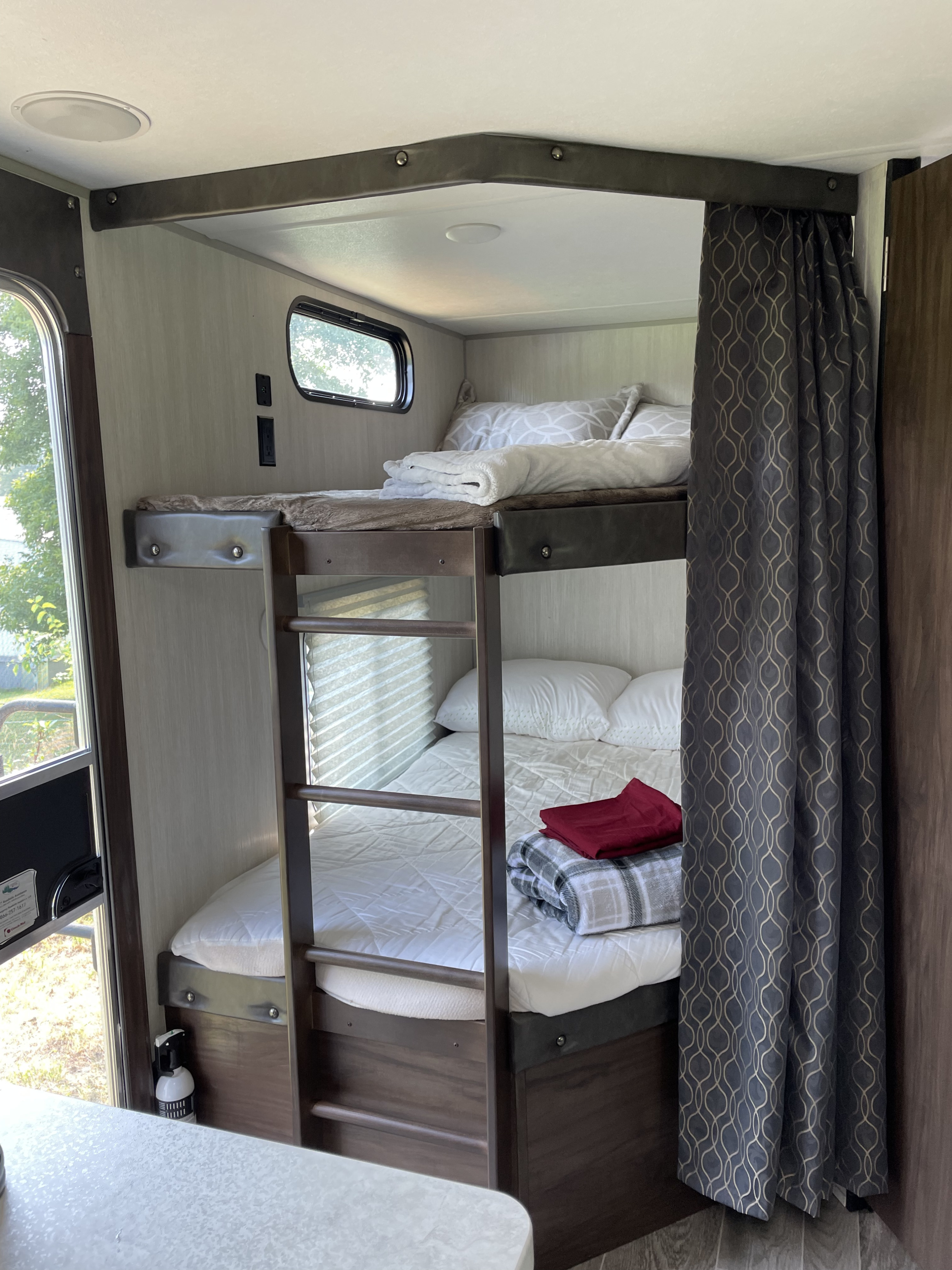 Bunk beds within an RV rental, showing comfortable bedding, privacy curtain, and interior details for travel.. Forest River 264DBH 2019