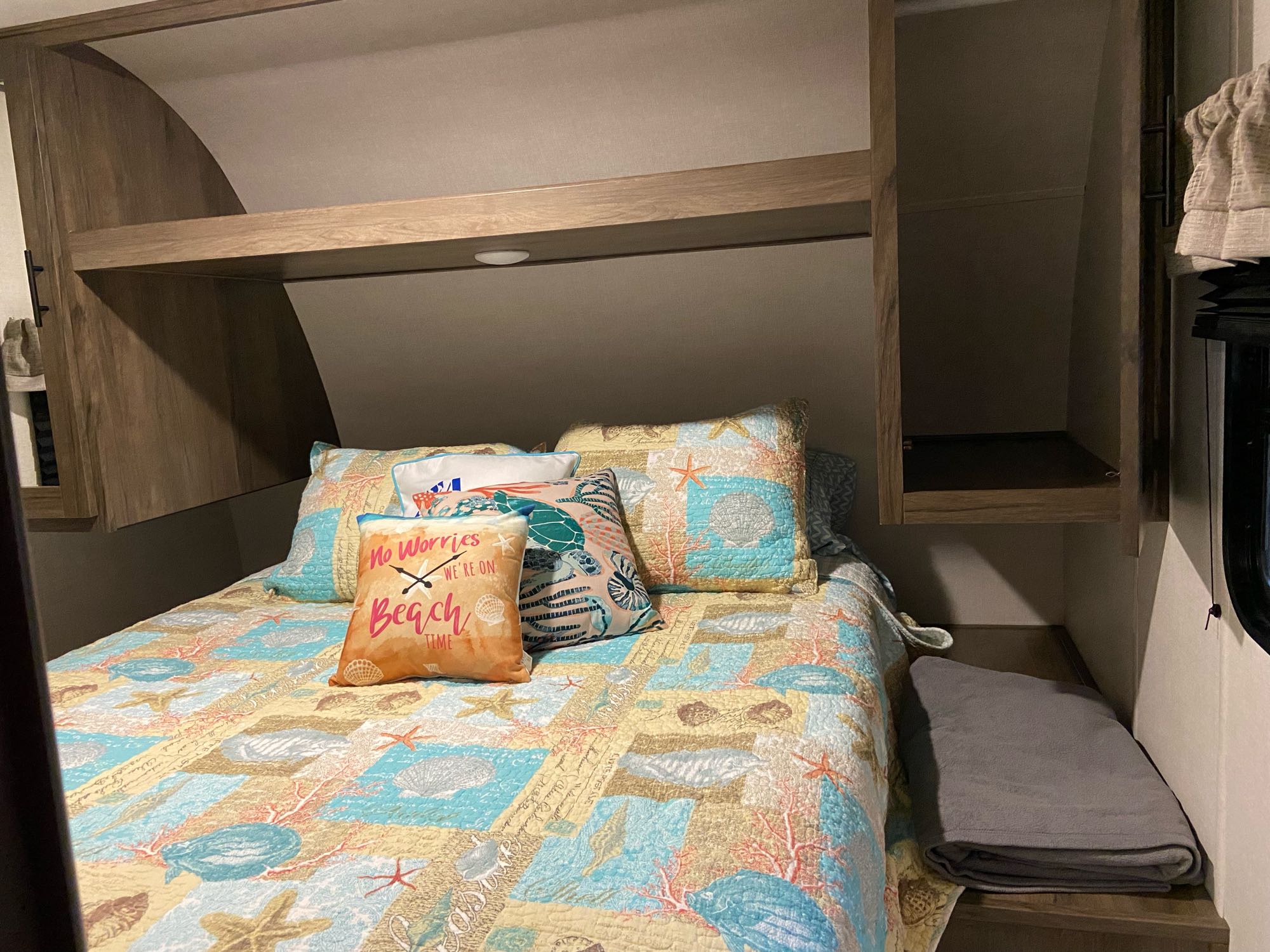 Inviting RV rental bedroom interior with a beach-themed bed, decorative pillows, and built-in overhead storage.. Prime Time Avenger 2021