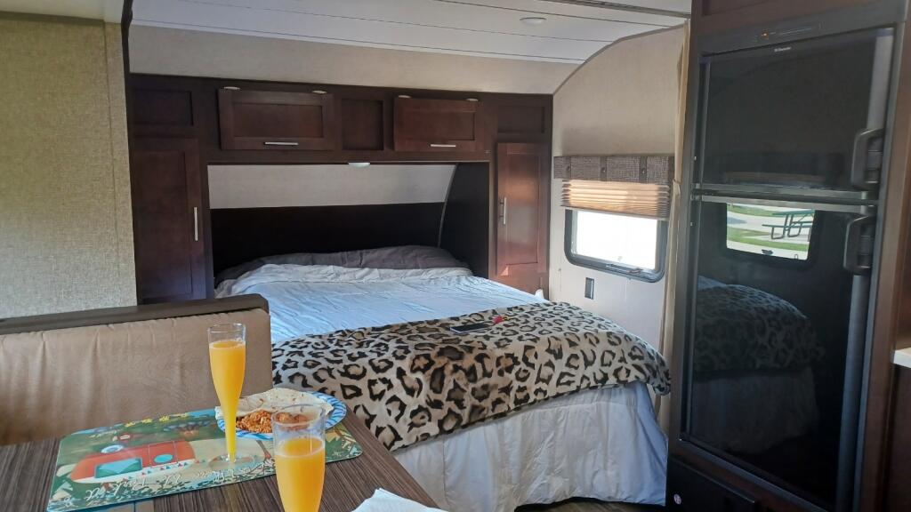 RV rental interior: bedroom with dark wood cabinetry and a leopard print blanket, plus a dining area with breakfast.. Forest River Cherokee Grey Wolf 2016
