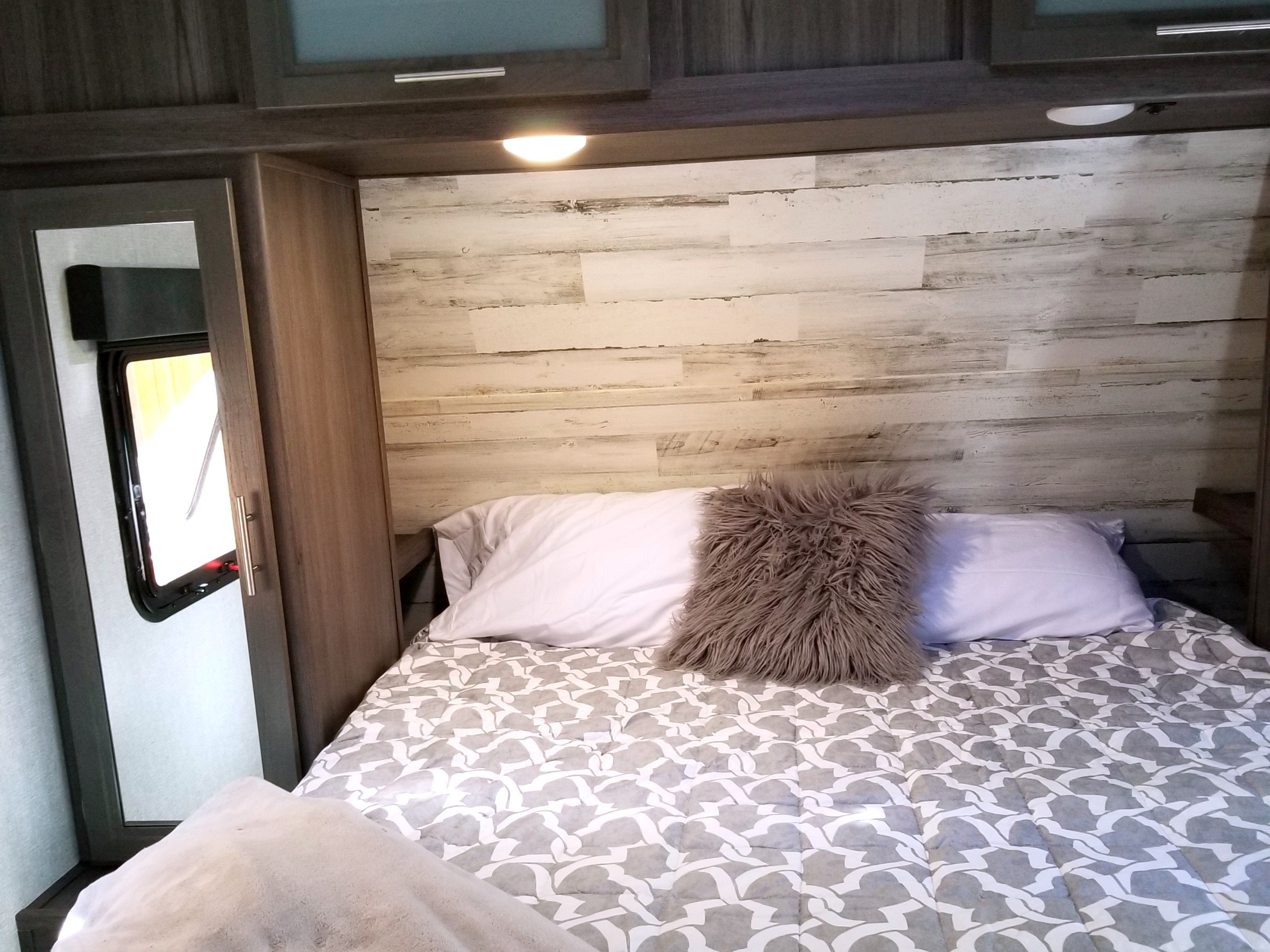 Cozy RV rental bedroom featuring a bed with patterned comforter, fluffy pillow, distressed wood paneling, and window.. Dutchmen Kodiak 2021