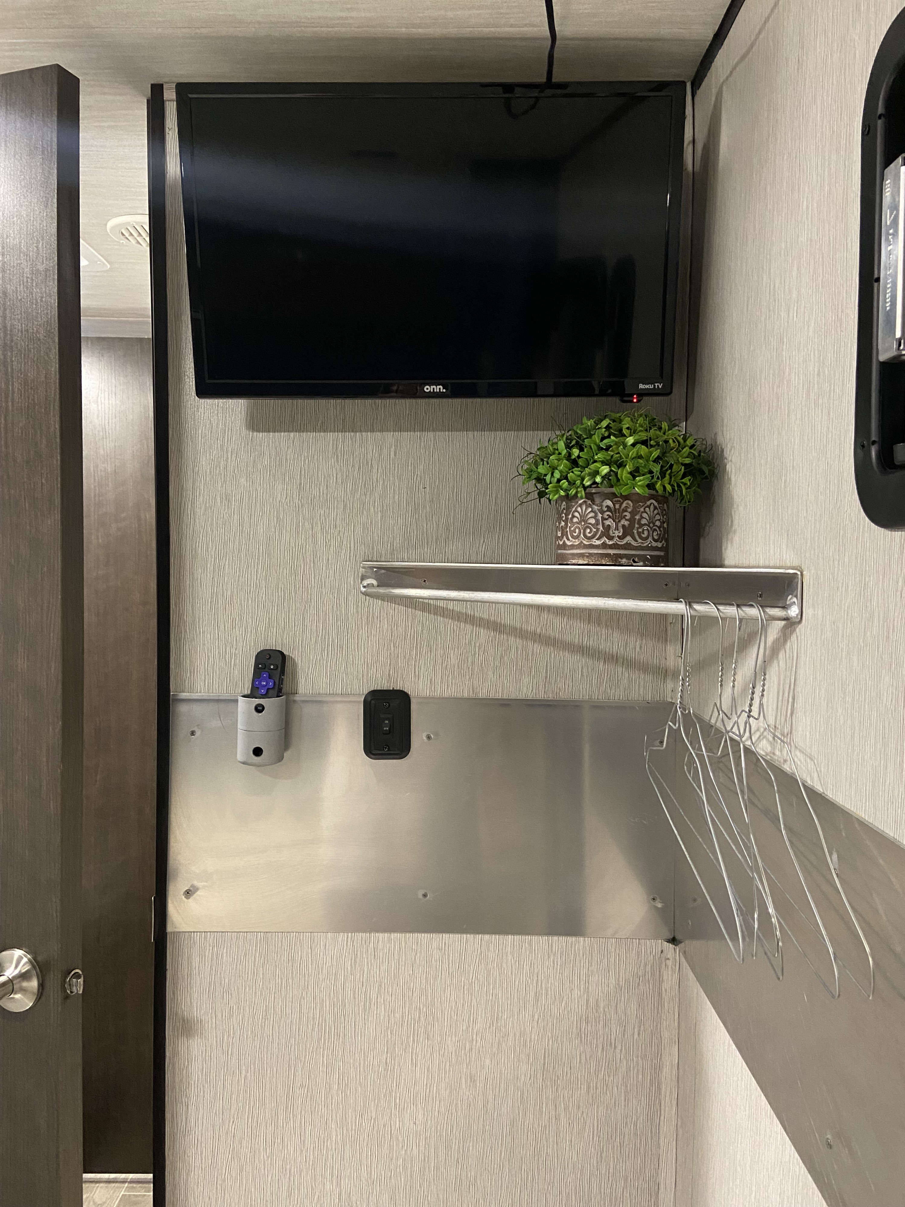 RV rental space: wall-mounted TV, plant, and smart storage solutions like hangers and a remote holder for efficiency.. Heartland Trail Runner 2020