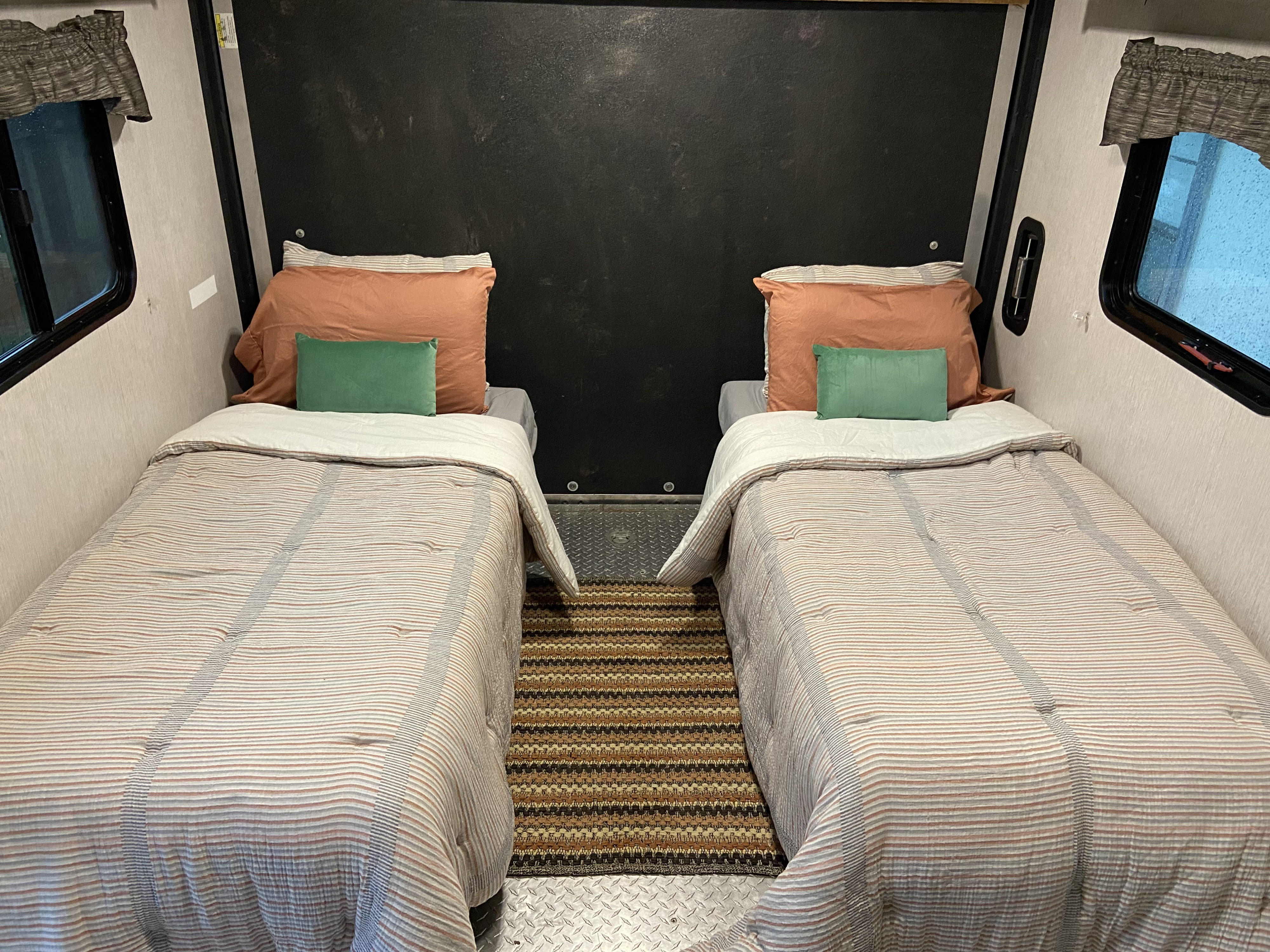 Cozy twin beds inside an RV rental, featuring striped bedding, colorful pillows, and a patterned rug on a diamond plate floor.. Heartland Trail Runner 2020
