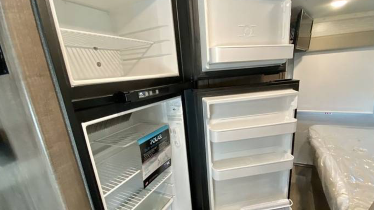 RV rental interior features an open refrigerator, showing empty freezer and fridge compartments with white shelves.. Winnebago Minnie Winnie 2020