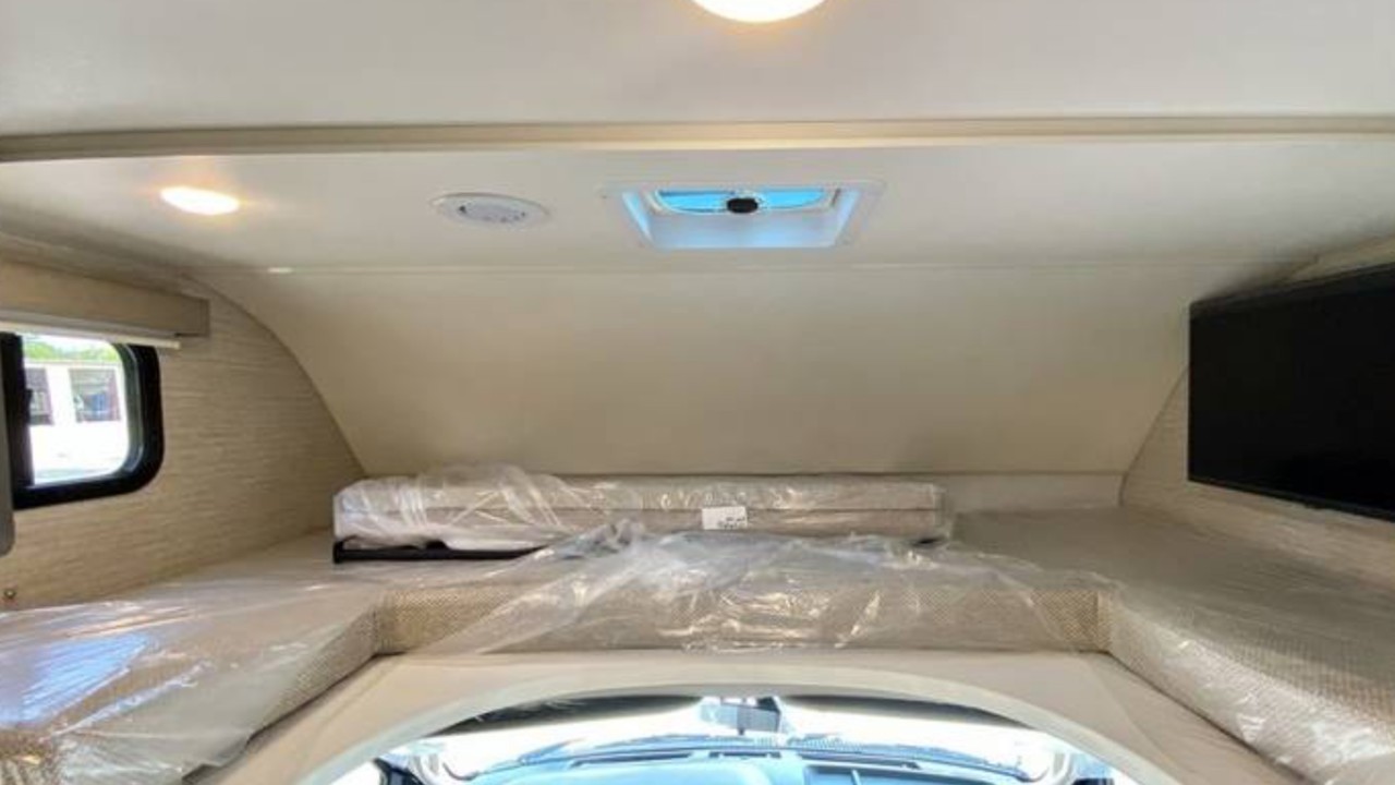 RV rental interior: A bright cab-over bunk with plastic-covered mattresses, window, and TV, perfect for rest.. Winnebago Minnie Winnie 2020