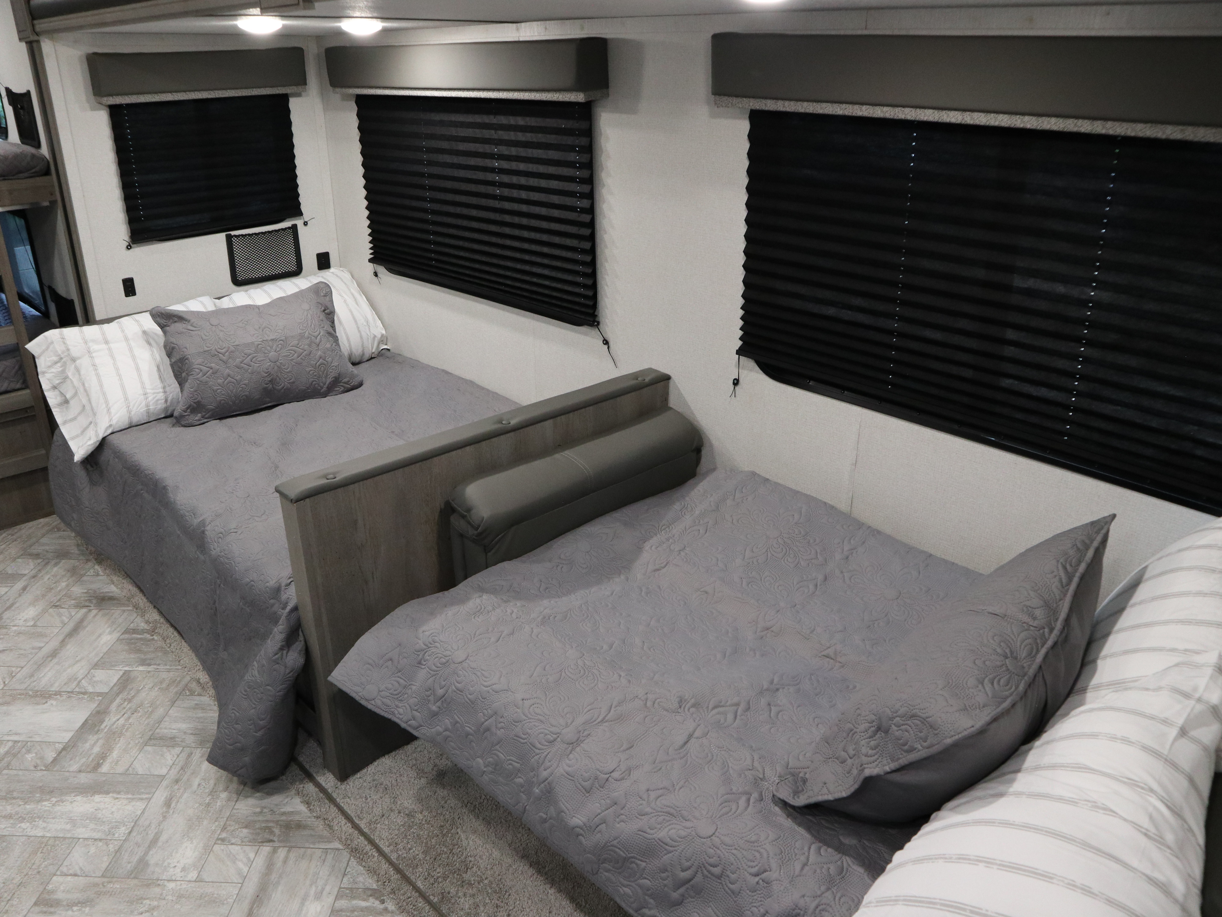 Cozy RV rental bedroom with two beds, grey quilted bedding, and black pleated privacy blinds for a comfortable stay.. Keystone Springdale 2021