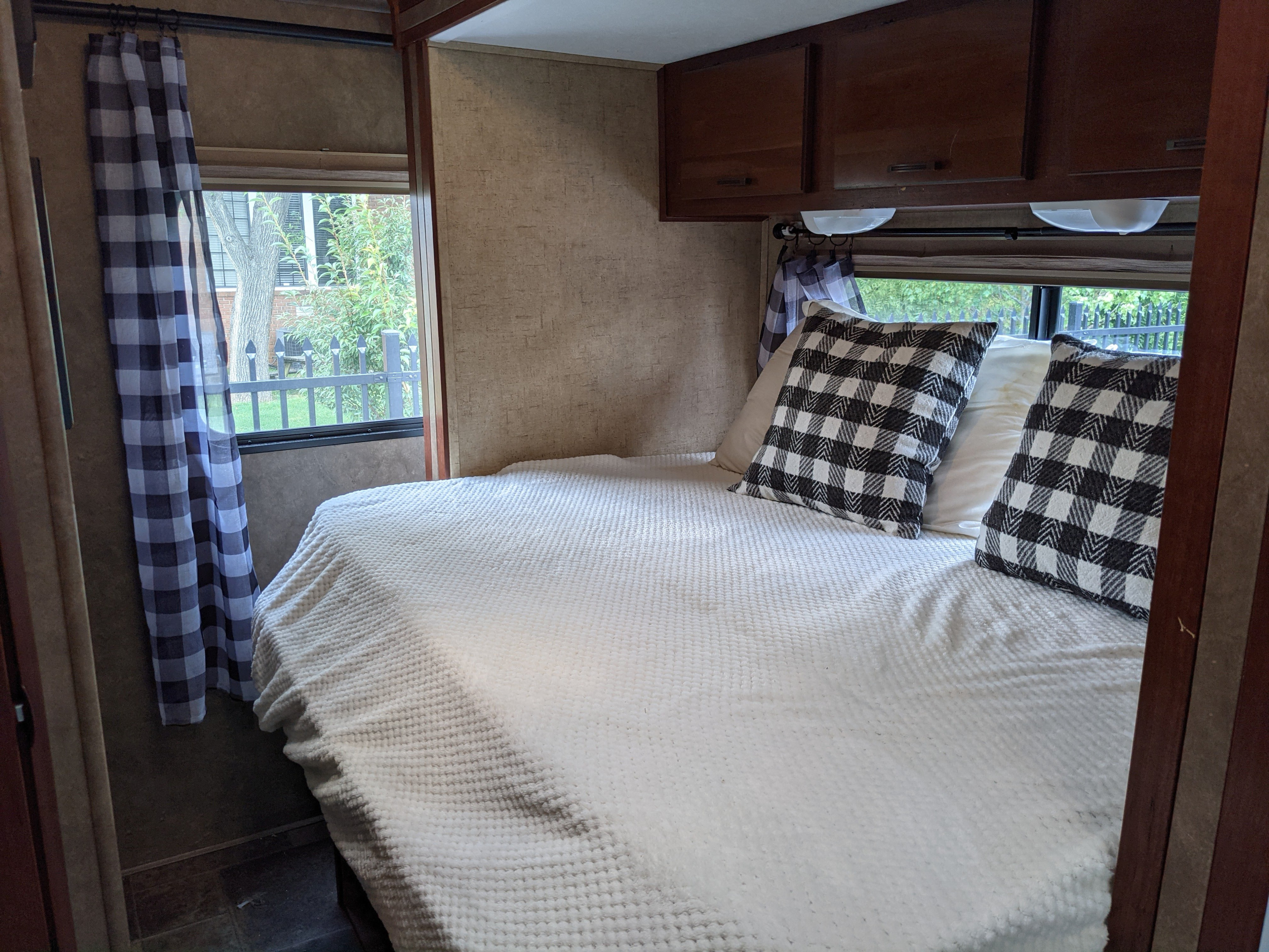 Cozy RV rental bedroom with bed, plaid pillows, curtains, and overhead cabinets for a comfortable stay.. Forest River Forester 2016