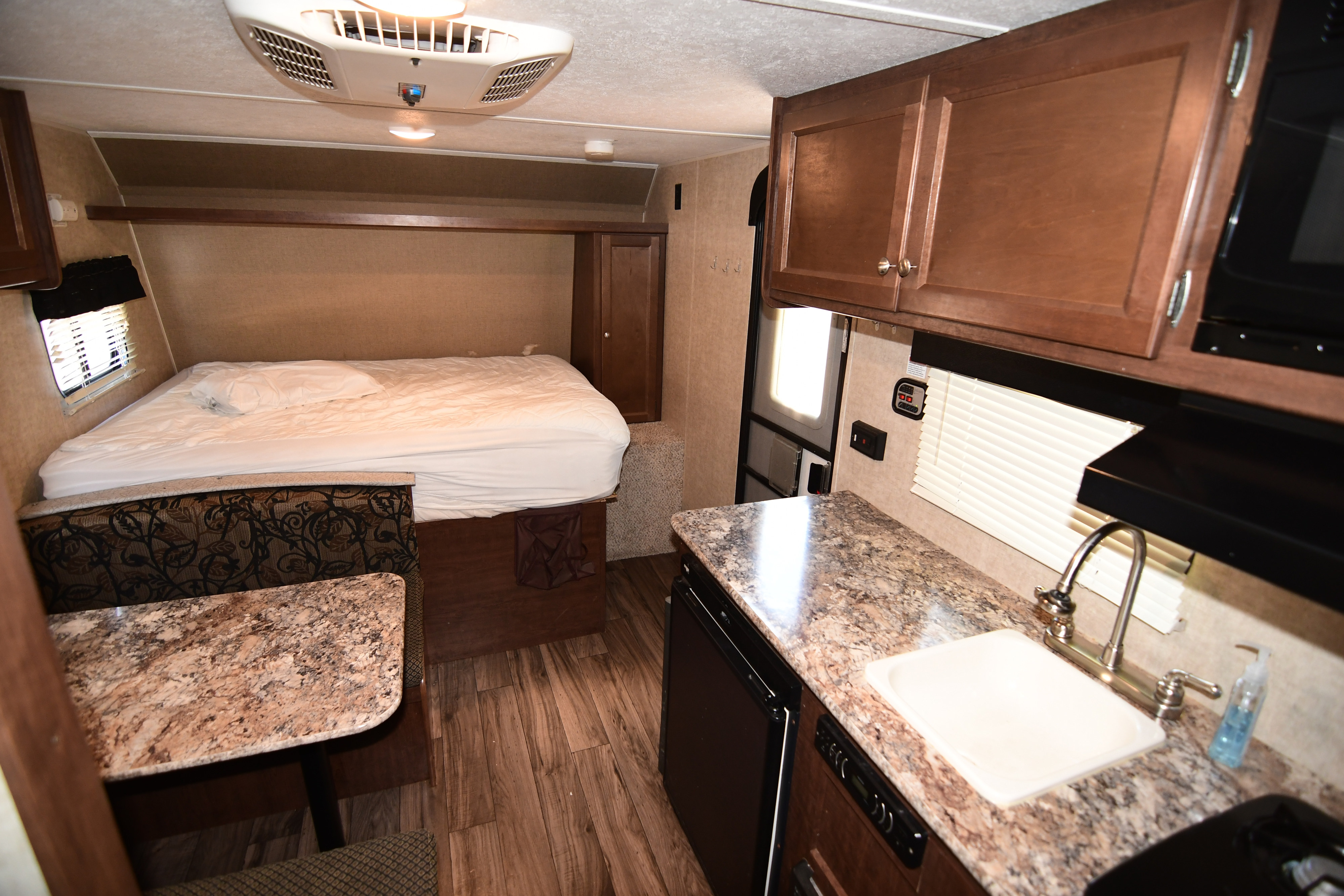 Cozy RV rental interior featuring a comfortable bed, functional kitchen with sink, dining area, and overhead cabinets.. Keystone RV Hideout 2017