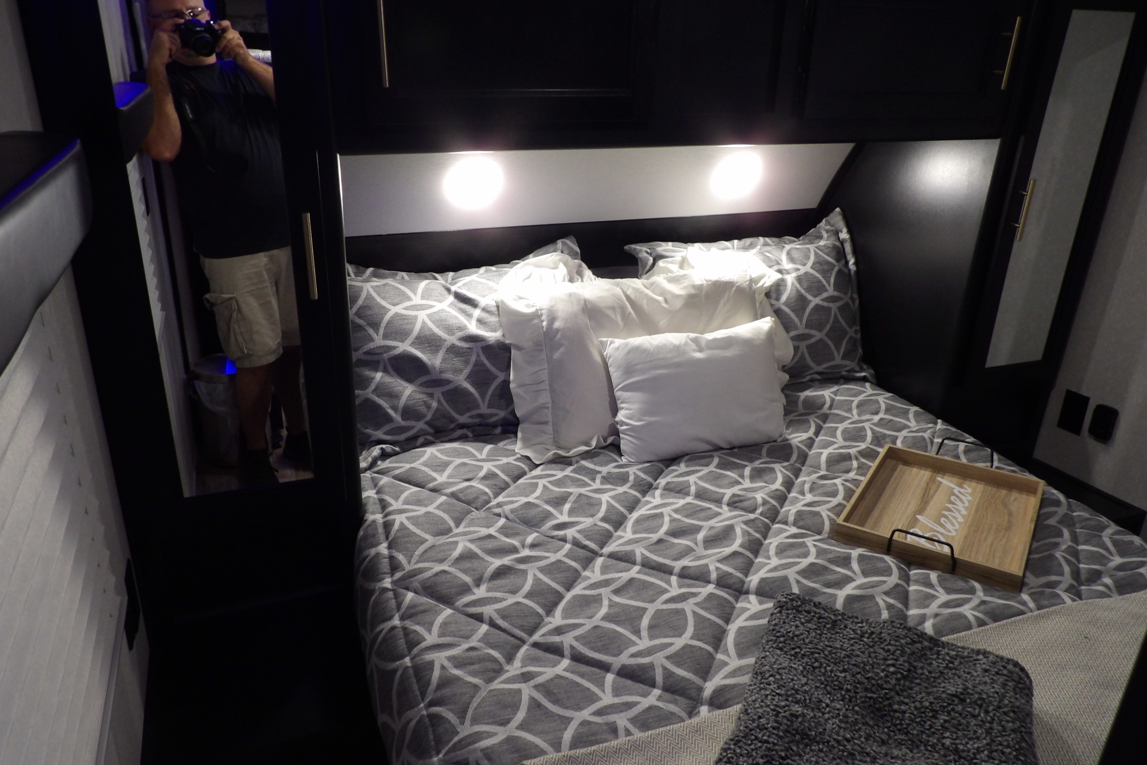 Cozy RV rental bedroom with patterned bedding & white pillows. Photographer's reflection in mirror taking the shot.. Forest River Cherokee Grey Wolf 2021