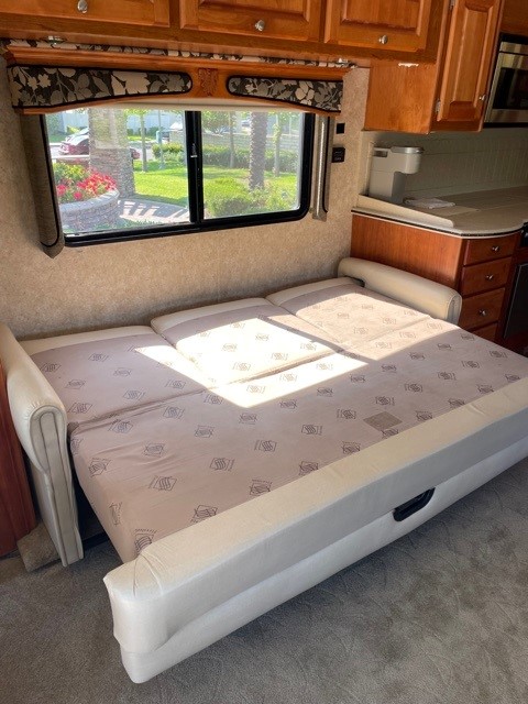 RV rental interior: a comfy sofa bed extends from beneath wooden cabinets, with a window offering a view of nature.. Monaco Diplomat 2006