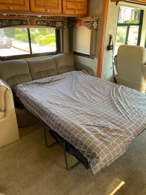 RV rental interior featuring a grey sofa bed with a plaid comforter, ready for guests. Wooden cabinets and windows complete the scene.. Monaco Diplomat 2006