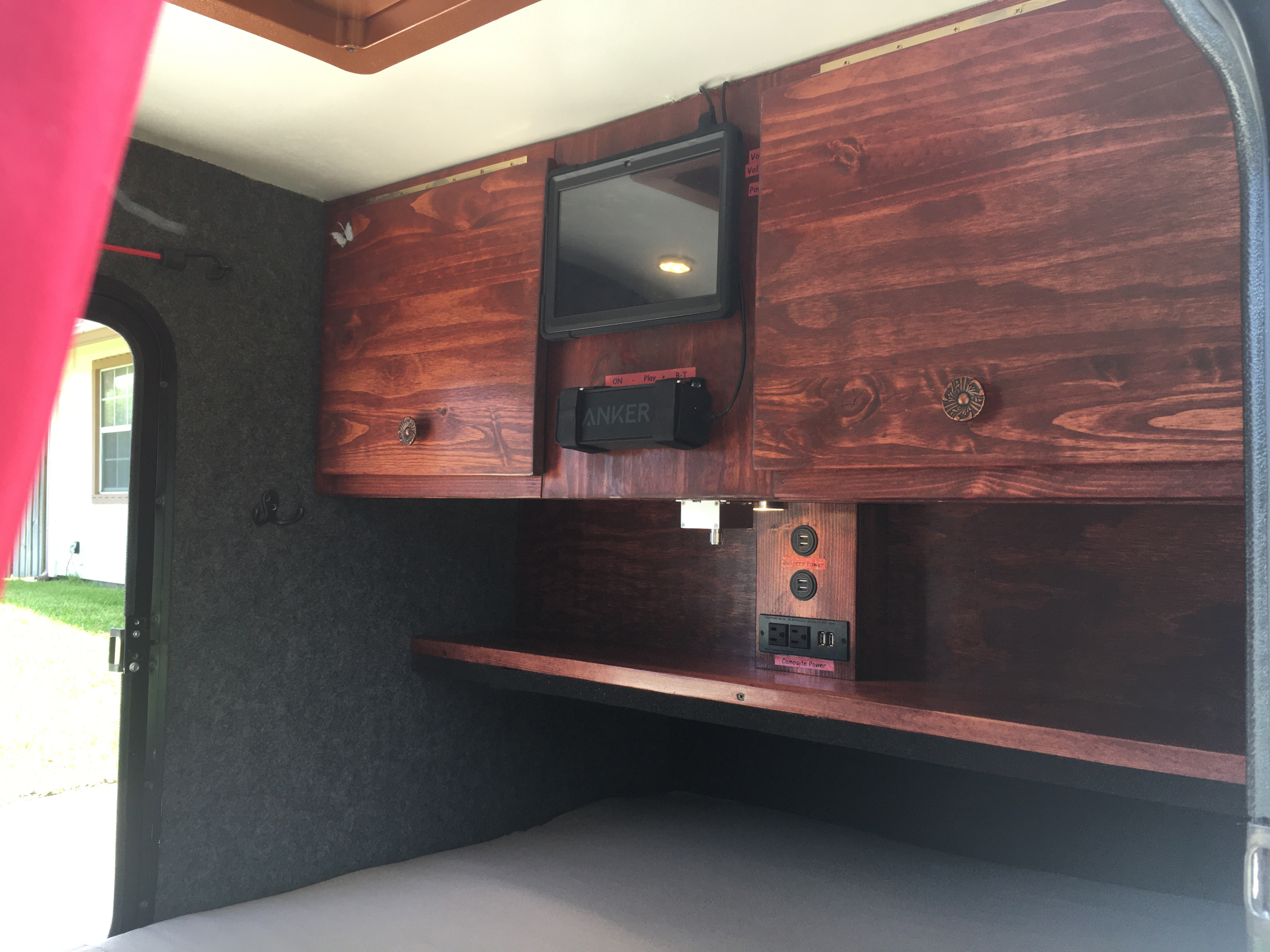 RV rental interior showing custom wood cabinets, TV, speaker, and charging station with 'Battery' & 'Campsite Power'.. Little Guy Teardrop Trailer 2007