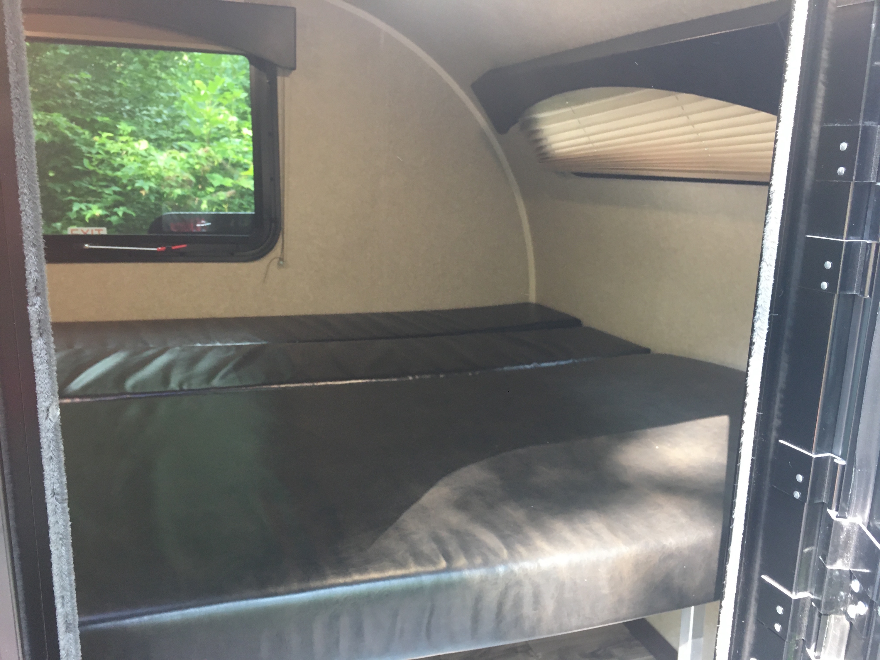 RV rental with dark bunk beds, window overlooking trees. A compact camper interior sleeping space.. Sunset Park Sunray 109 2021