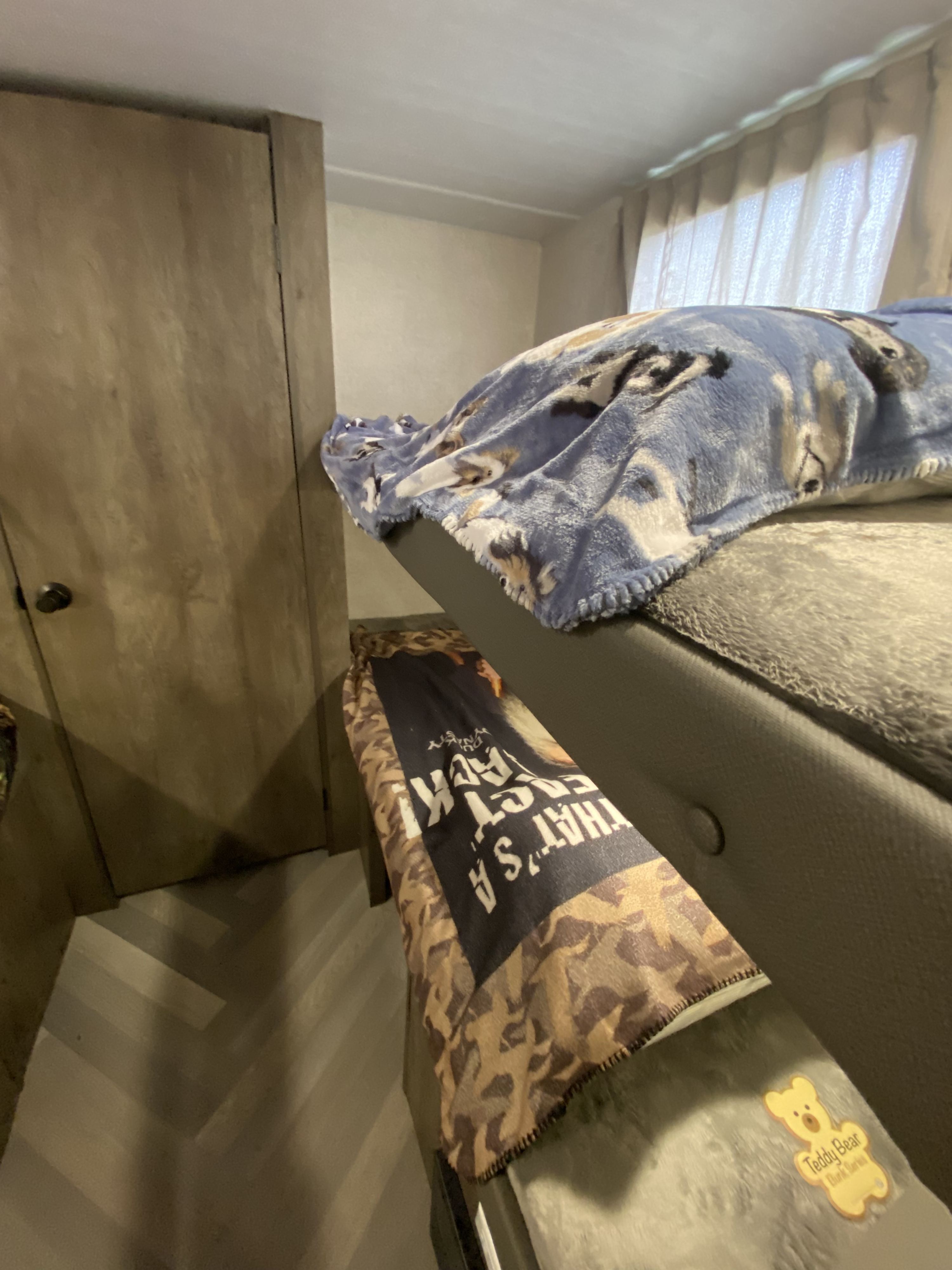 Inside an RV rental: a cozy bunk bed with a blue wolf blanket, a camo blanket on the lower area, and a wood cabinet.. Forest River Wildwood 2021