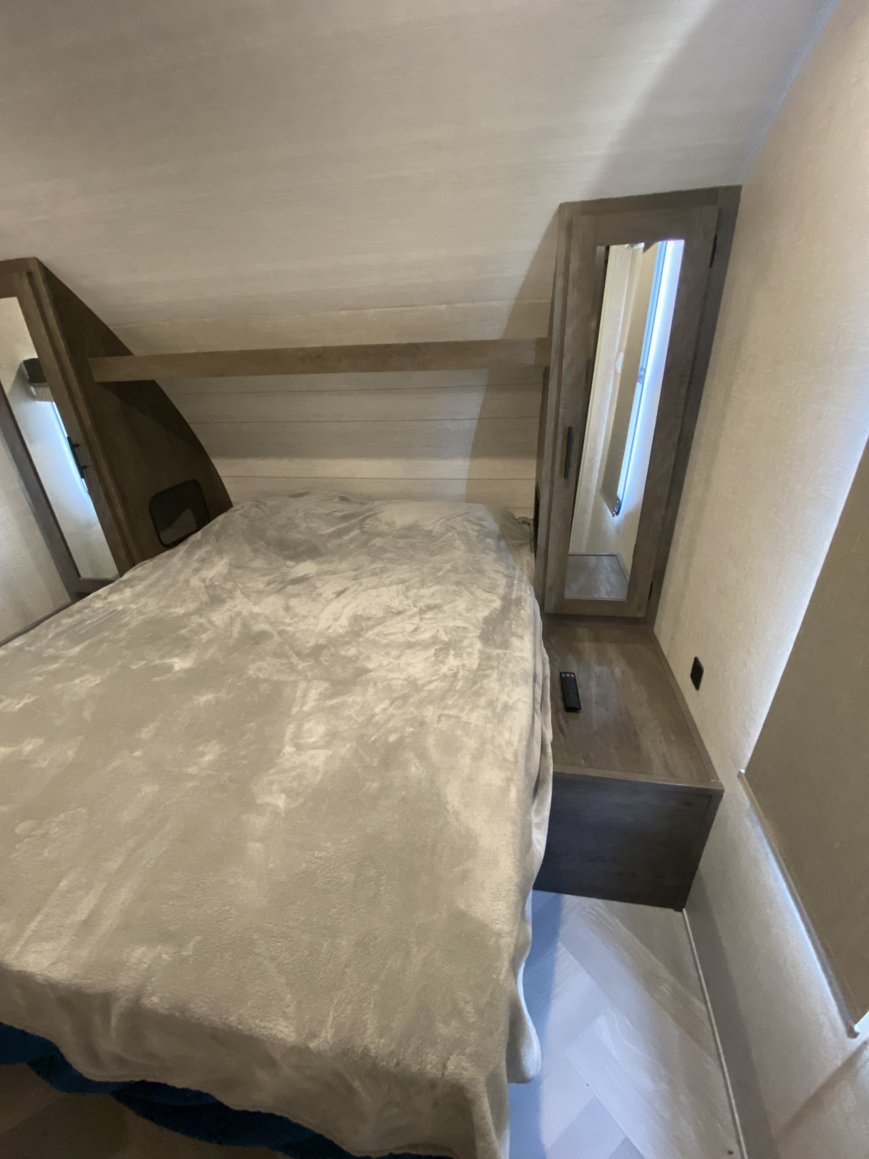 Cozy RV rental bedroom with a comfortable bed, plush blanket, built-in mirrored cabinets, and modern shiplap accents.. Forest River Wildwood 2021