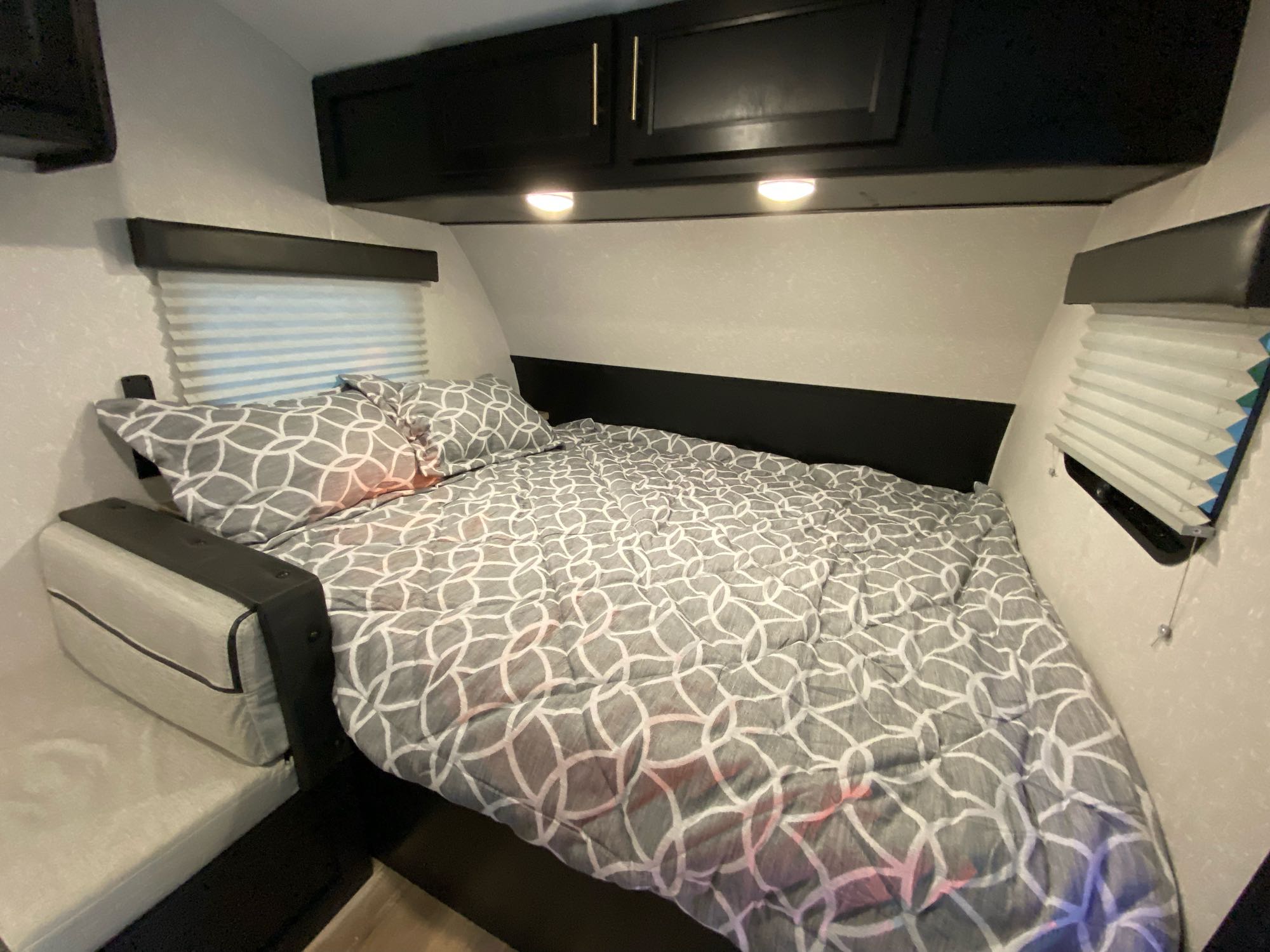 Cozy RV rental bedroom featuring a bed with patterned comforter, overhead cabinets, and windows with blinds.. Forest River Other 2021