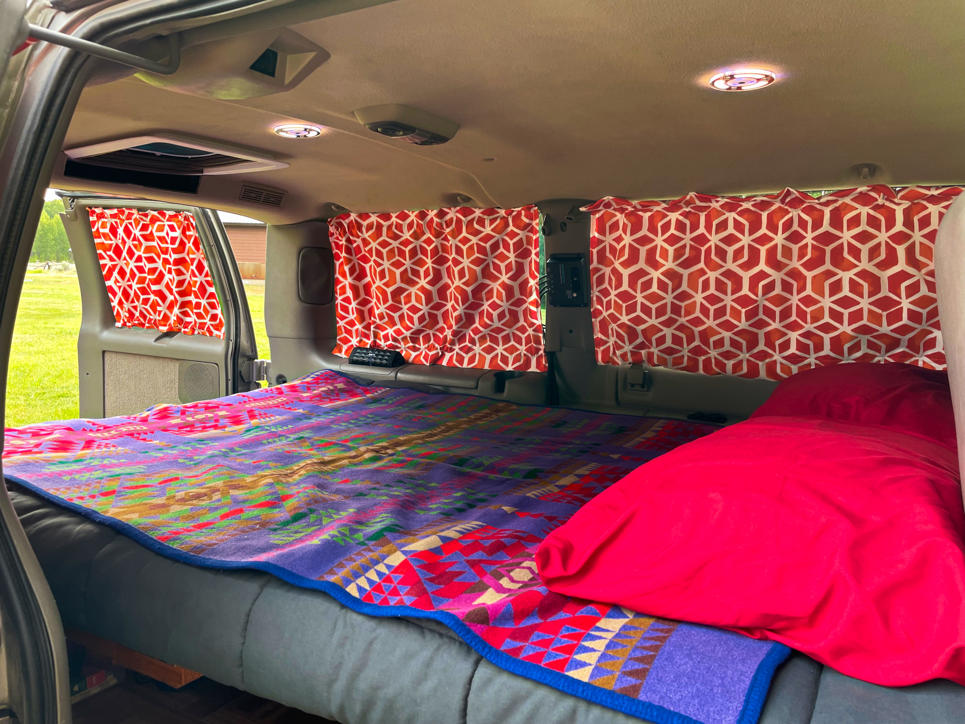 Inside a cozy RV rental: colorful blanket, bright pink bedding, patterned curtains, and ceiling fan in a converted van.. Gmc Other 2004
