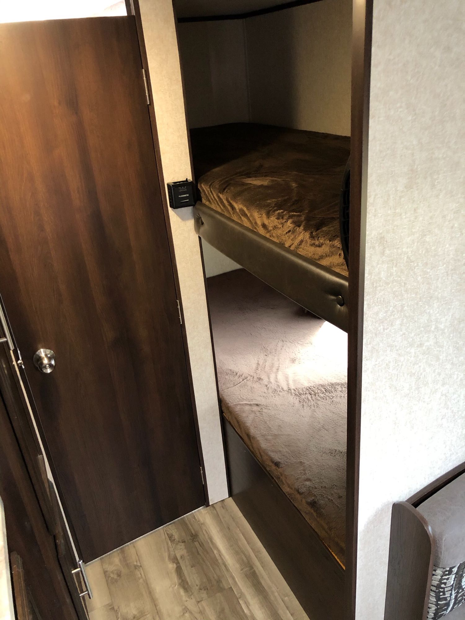 Inside an **rv rental**: dark wood door opens to cozy bunk beds with blankets. A Dometic control is on the wall.. Jayco Jay Flight 2019