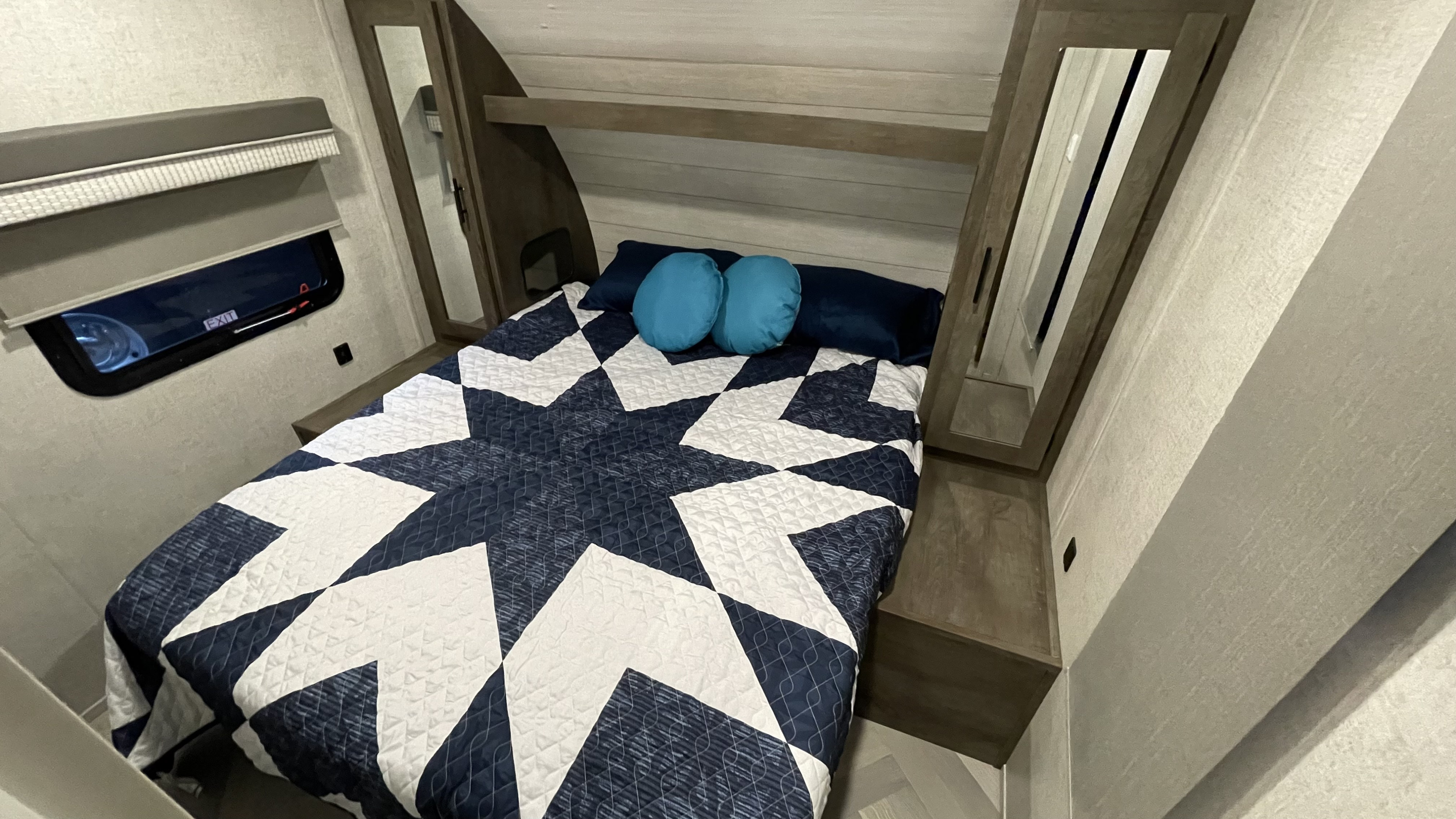 Cozy RV rental bedroom featuring a blue and white star quilt, pillows, side cabinets with mirrors, and a window.. Forest River Salem Cruise Lite 2021