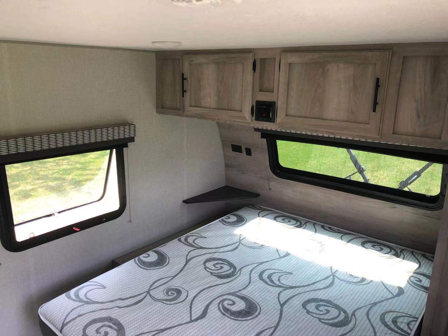 This RV rental shows a cozy bedroom interior with a patterned mattress, two windows, and overhead cabinets. Perfect for travel.. K-Z Manufacturing Escape 2021