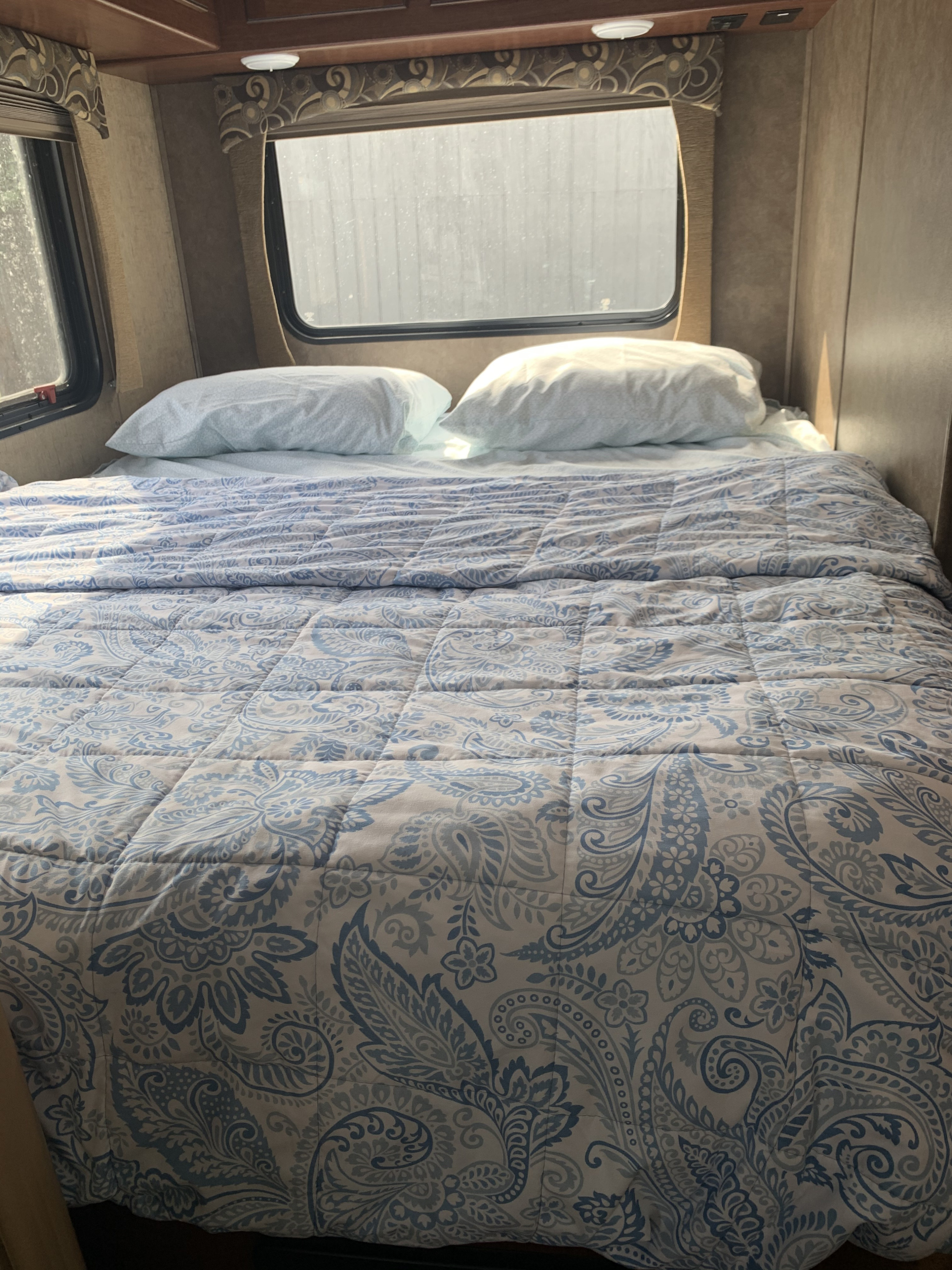 Cozy bedroom in an RV rental, featuring a bed with a blue paisley comforter and bright windows.. Forest River Sunseeker 2016