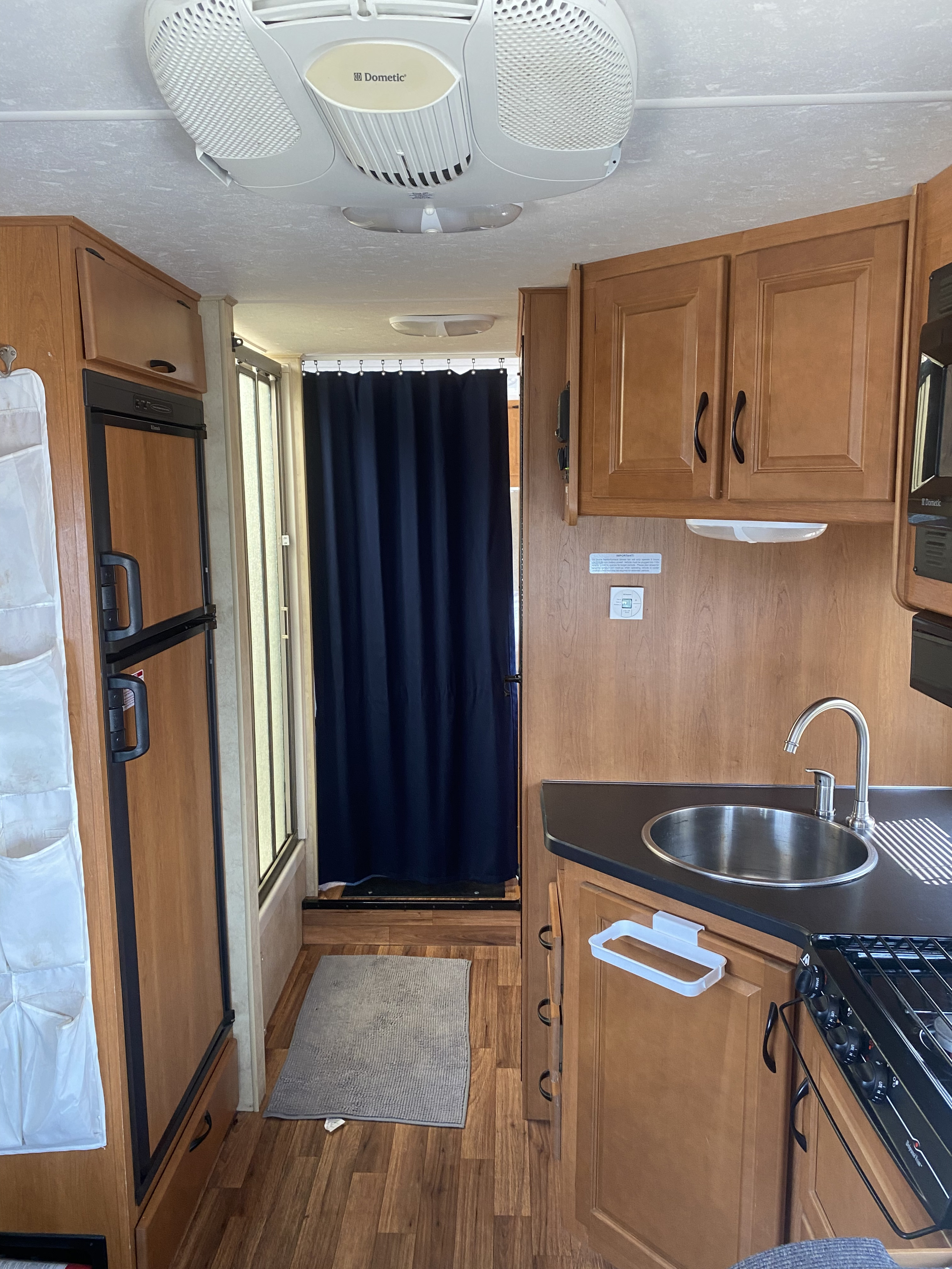 Inside an RV rental: a compact kitchen with sink, stovetop, refrigerator, and a dark blue privacy curtain.. Thor Motor Coach Four Winds Majestic 2012