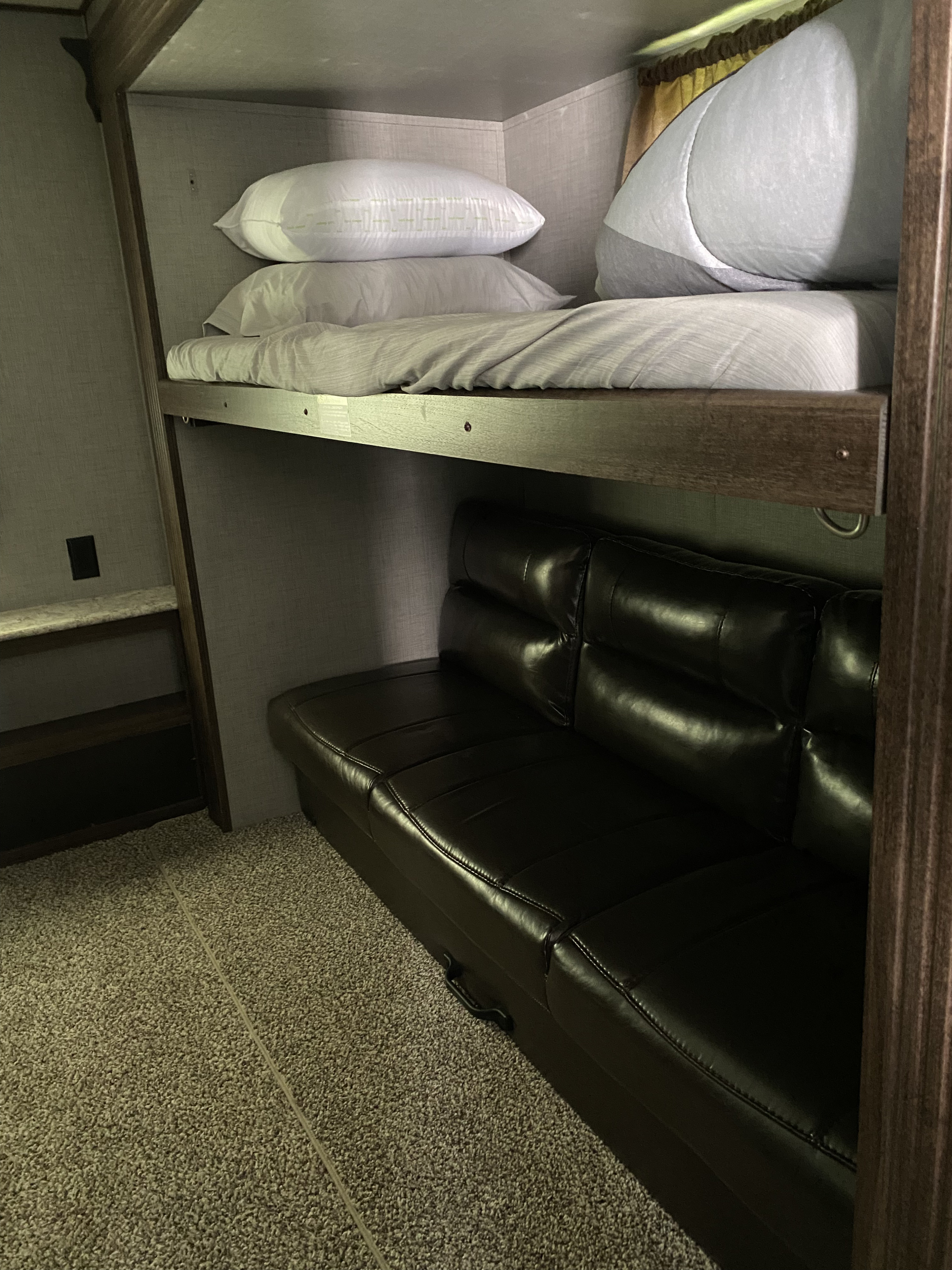 Inside an RV rental: a comfortable top bunk with bedding over a dark leather sofa. Features include textured walls and carpet.. Crossroads Zinger 2018