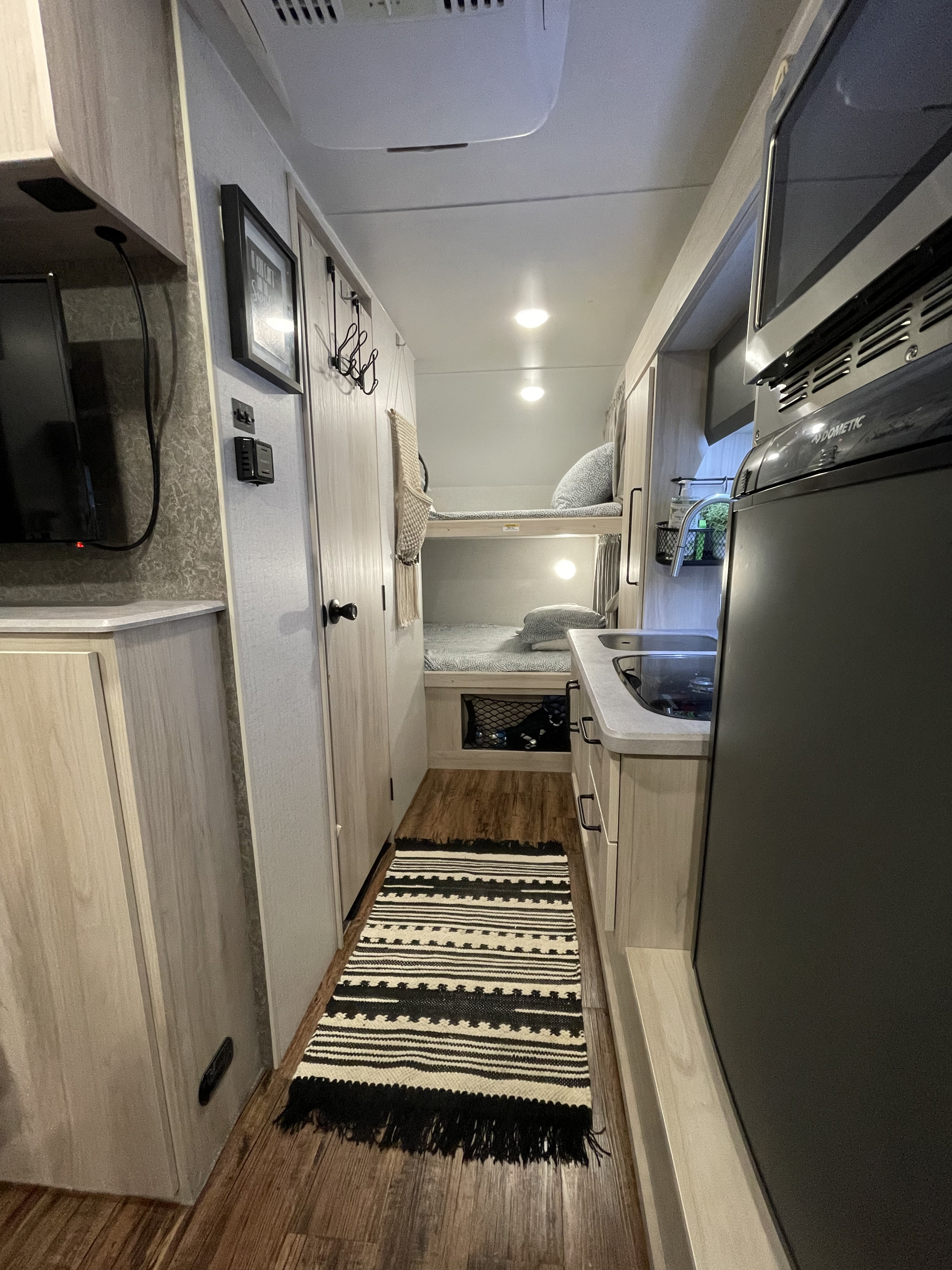 Inside an rv rental: a cozy hallway with bunk beds, a compact kitchen, and a patterned rug on wood flooring.. Winnebago Hike 2021