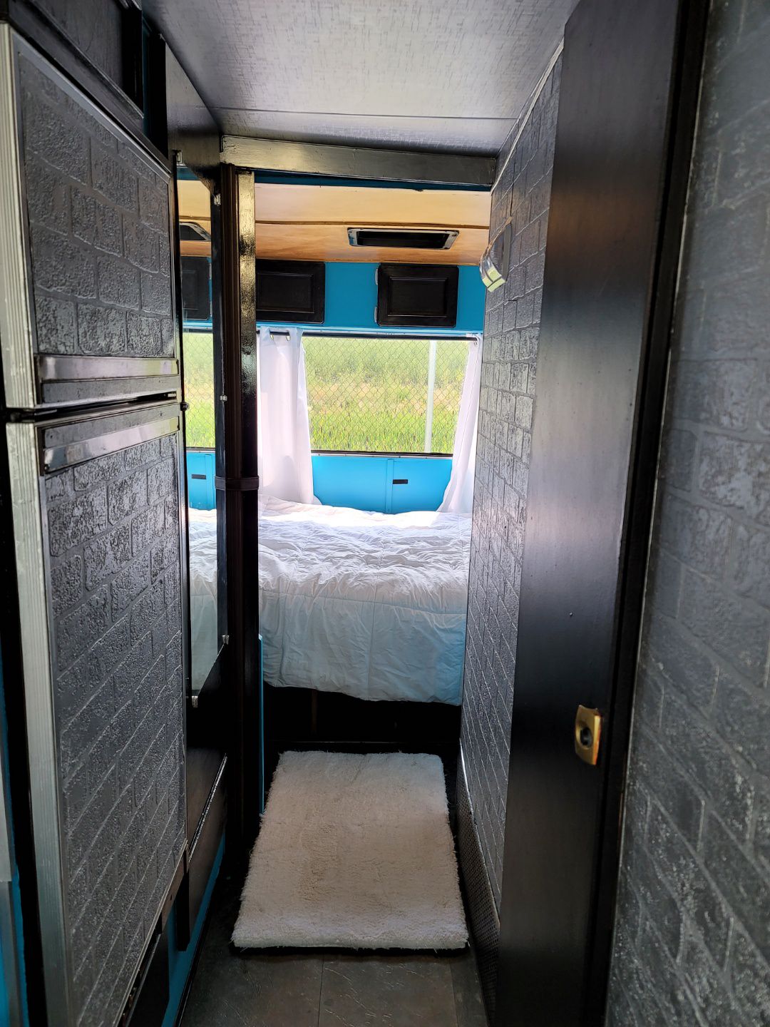 Cozy RV rental: Dark hallway leads to a bedroom with white bedding & a bright window view of green fields.. Chevrolet Other 1980