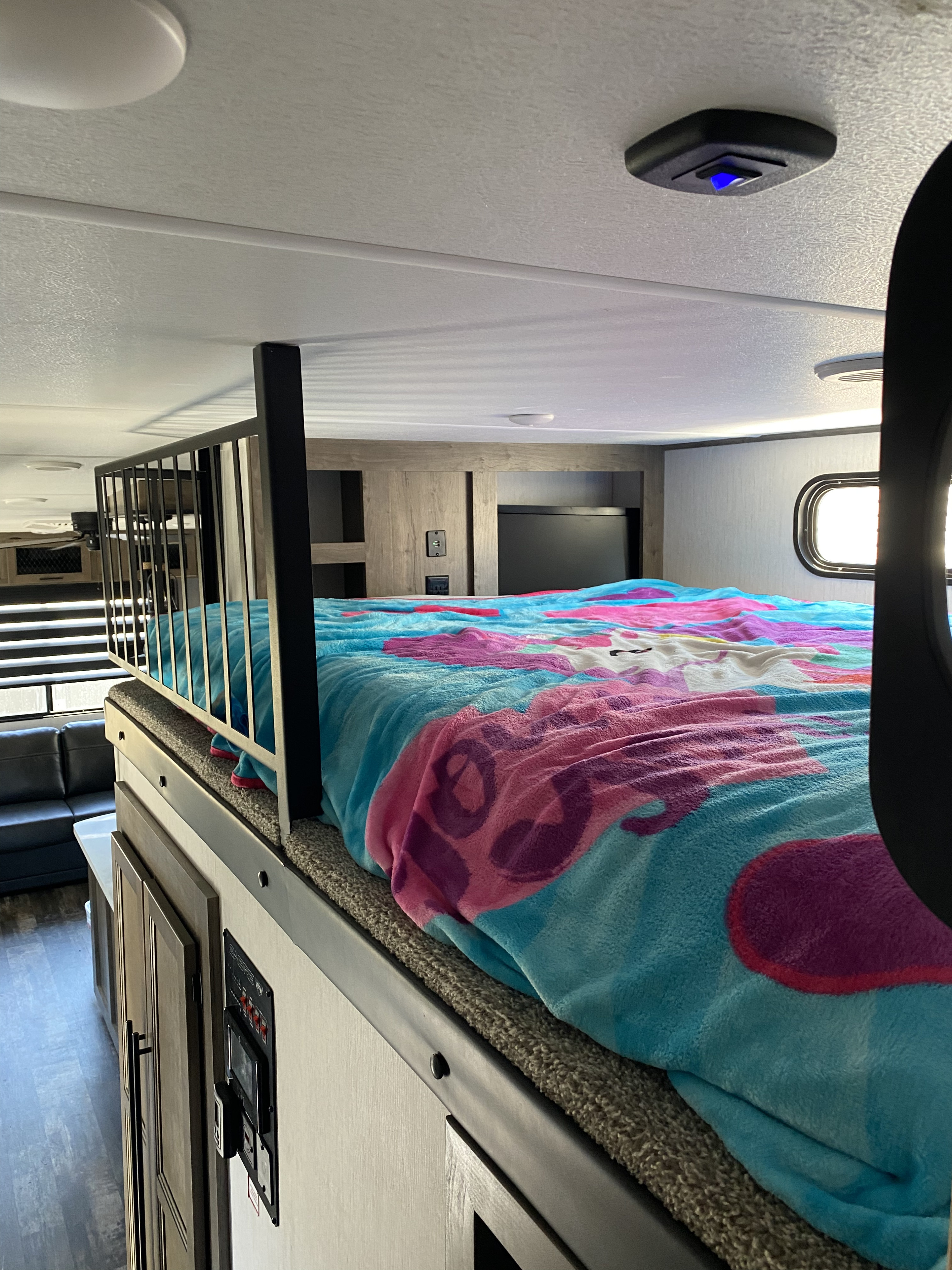 Cozy RV rental interior: a colorful unicorn blanket on a bunk bed with a railing, overlooking a spacious living area.. Forest River Other 2021