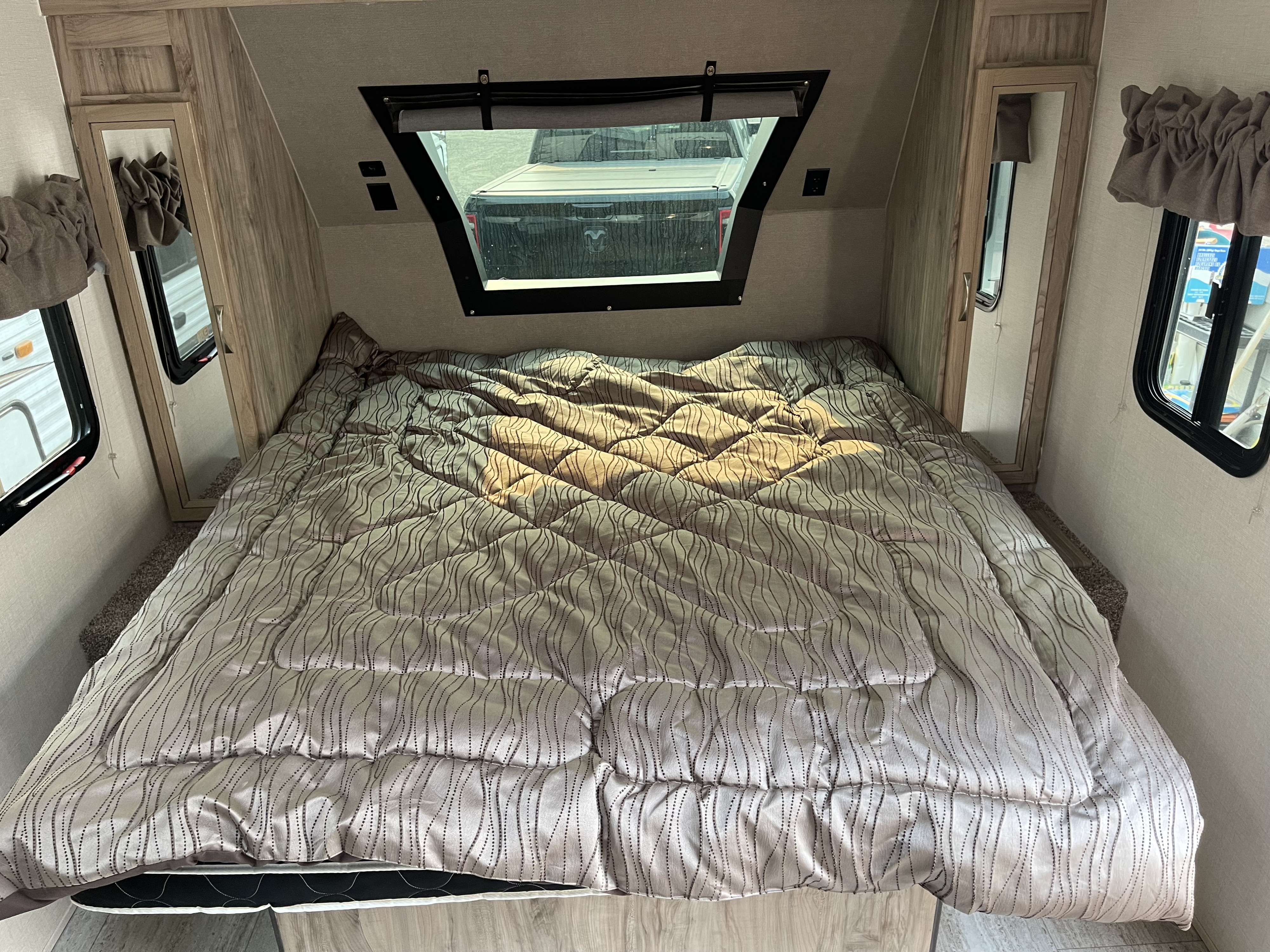 This RV rental showcases its comfortable bedroom with a patterned comforter, front window, and mirrored cabinet.. Solaire 211BH 2019