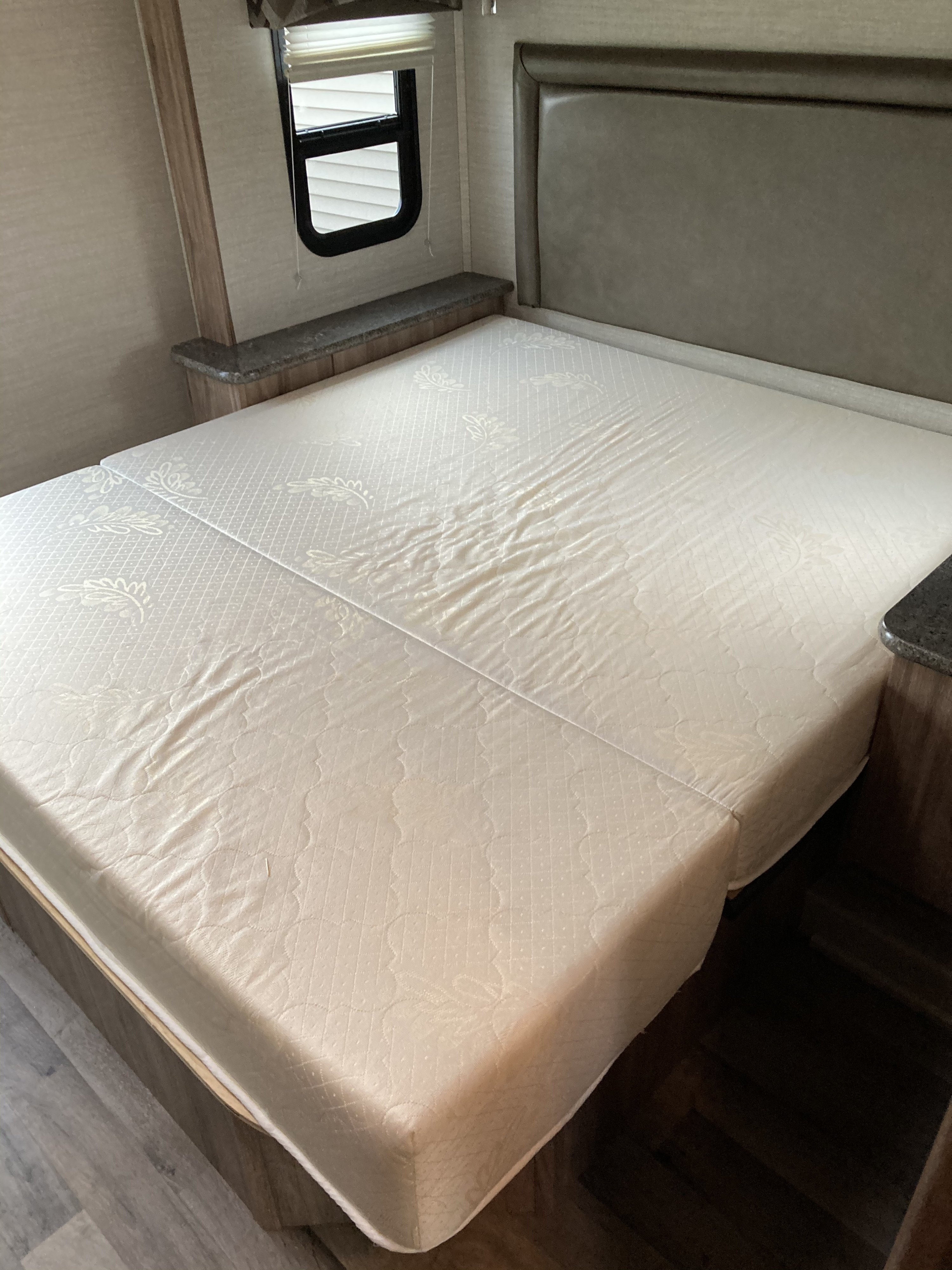 RV rental bedroom interior with a split mattress, headboard, and window, highlighting compact living space.. Jayco Redhawk 2020
