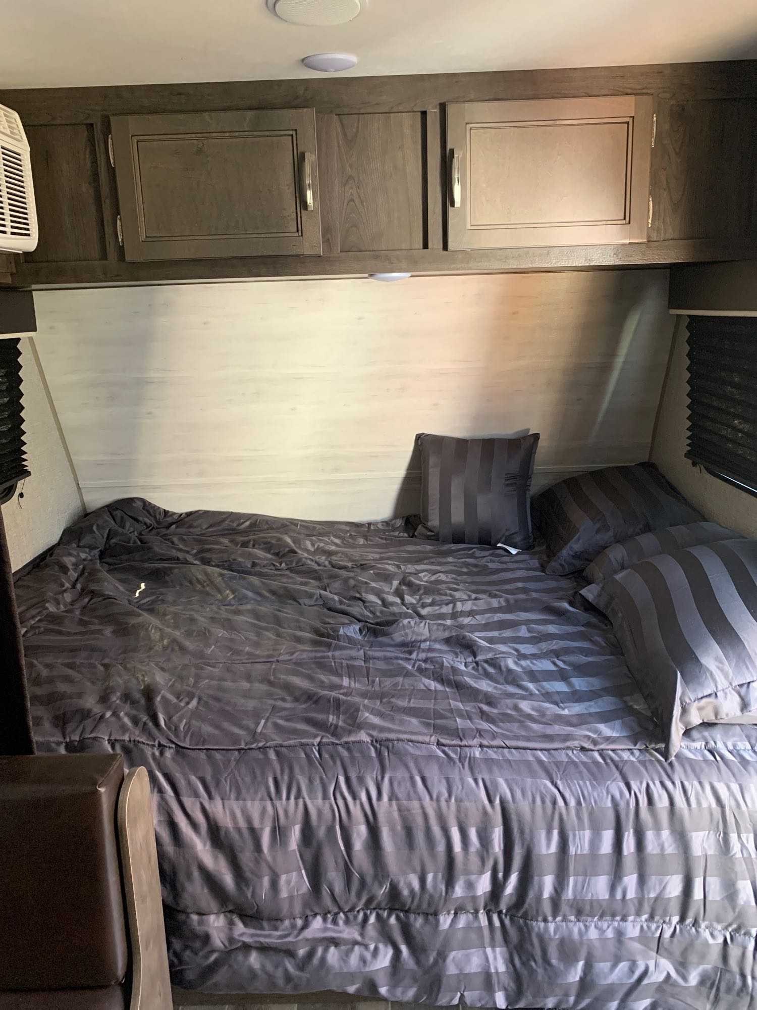 Inside an RV rental: a cozy bedroom with striped gray bedding, pillows, and wood-toned cabinets.. Jayco Jay Flight 2021