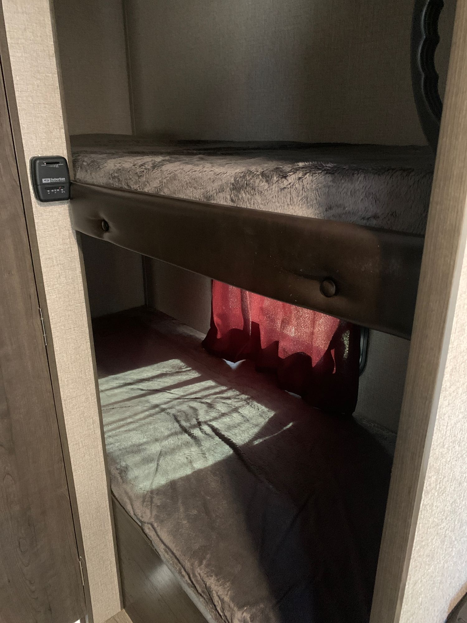 Cozy RV rental bunk beds with a red privacy curtain and sunlight streaming in. A thermostat is visible on the left.. Jayco Jay Flight 2021