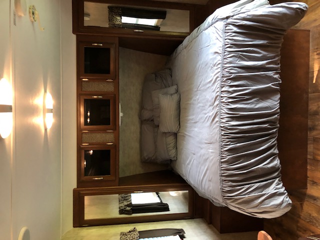 An RV rental's bedroom, showing a large bed with gray bedding, built-in mirrored cabinets, and wall sconces.. Keystone Passport 2015