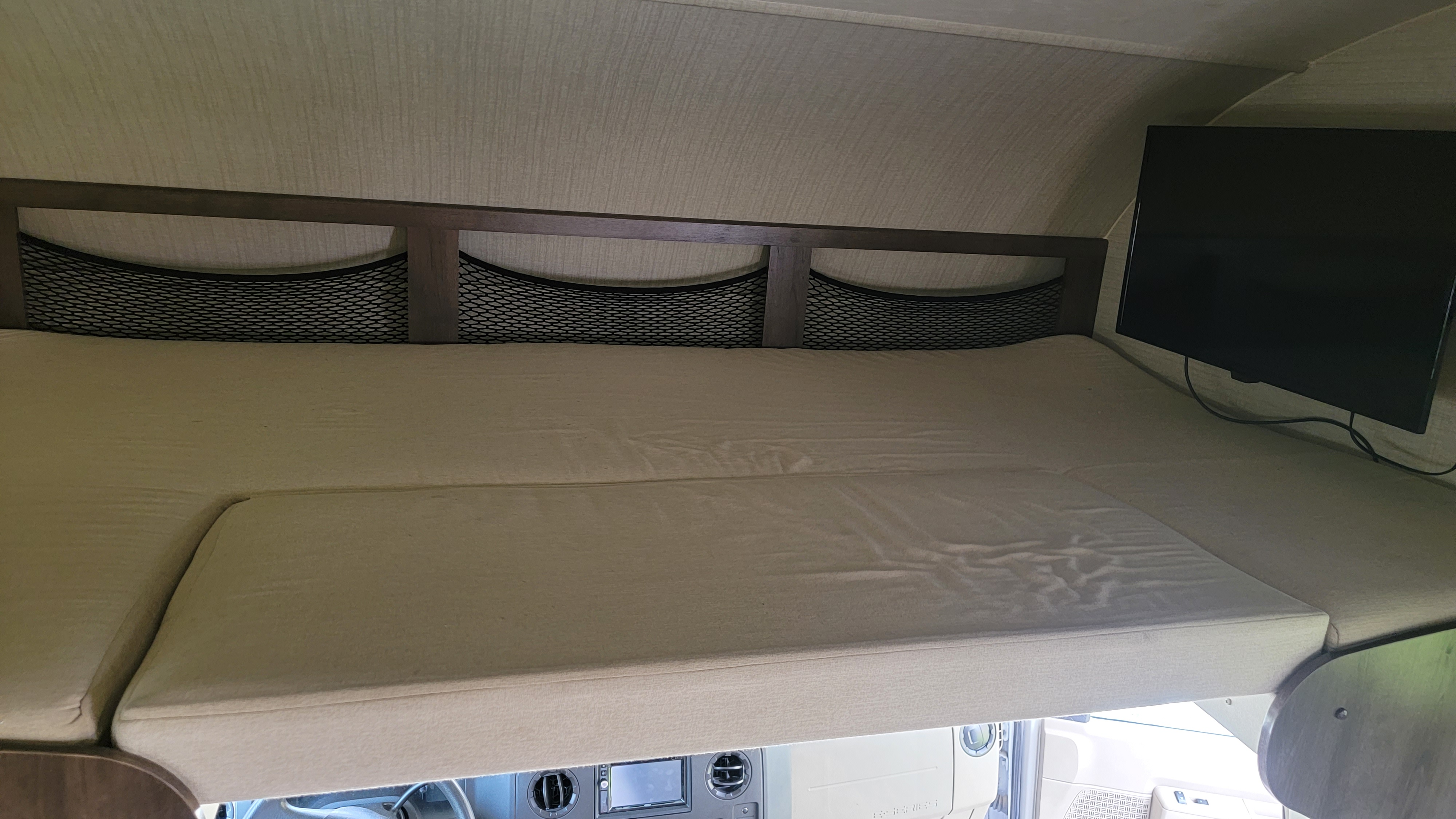 Spacious cab-over bunk sleeping area in an RV rental, complete with mattress, storage nets, and a mounted TV.. Jayco Redhawk 2018